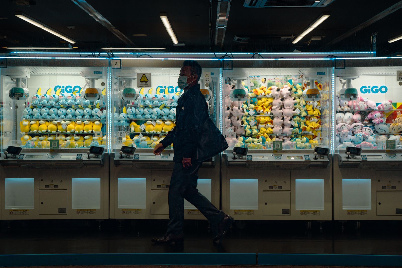 A lit wall of arcade cabinets at night, a single figure walking past — the kind of indoor evening a rainy-season week actually buys you.