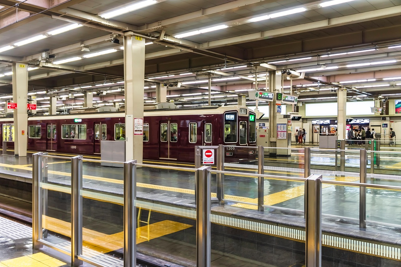 A long terminal platform under a white girder roof, maroon Hankyu trains at the far track.