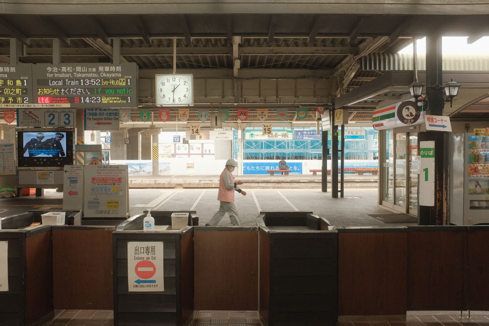 A quiet station concourse in Japan with a round clock above the ticket gates and one person walking through.