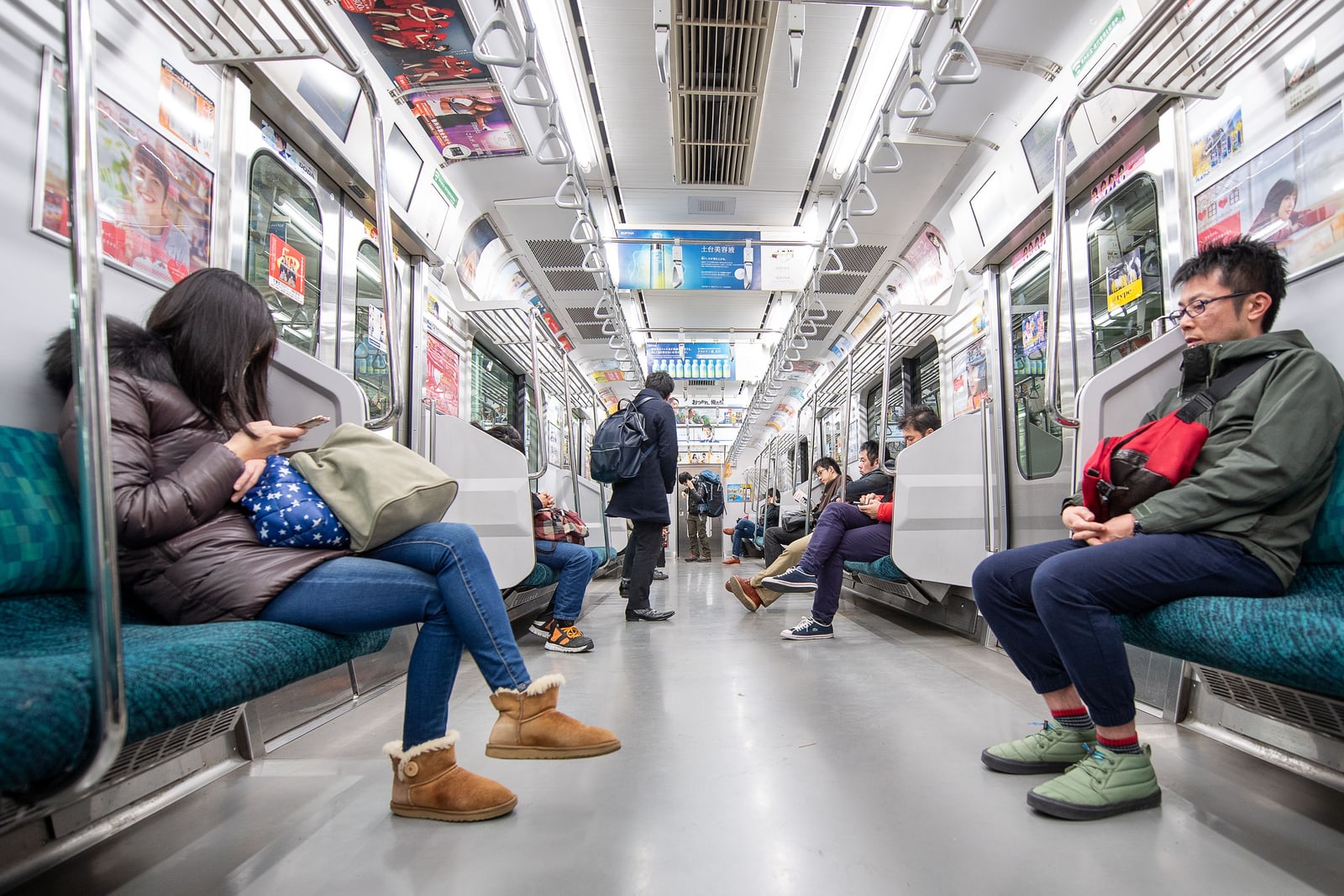 Two passengers in winter coats seated on green benches in a nearly empty Tokyo subway car.