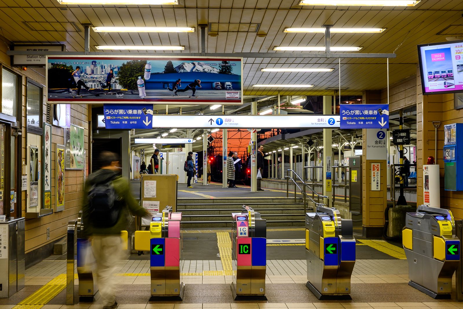 Ticket gates at a Japanese station at night with passengers passing through.