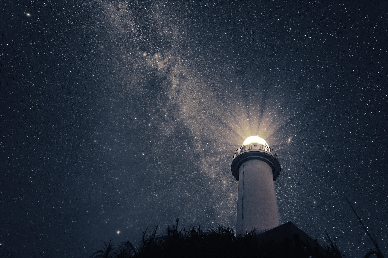 Looking up at a lit lighthouse tower under the Milky Way