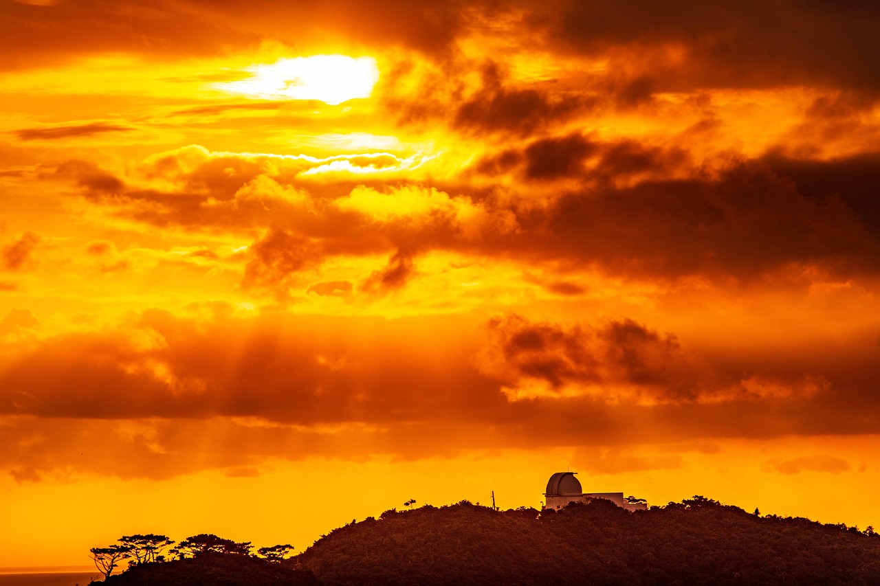 An orange sunset sky over a wooded hill with a small domed building on top