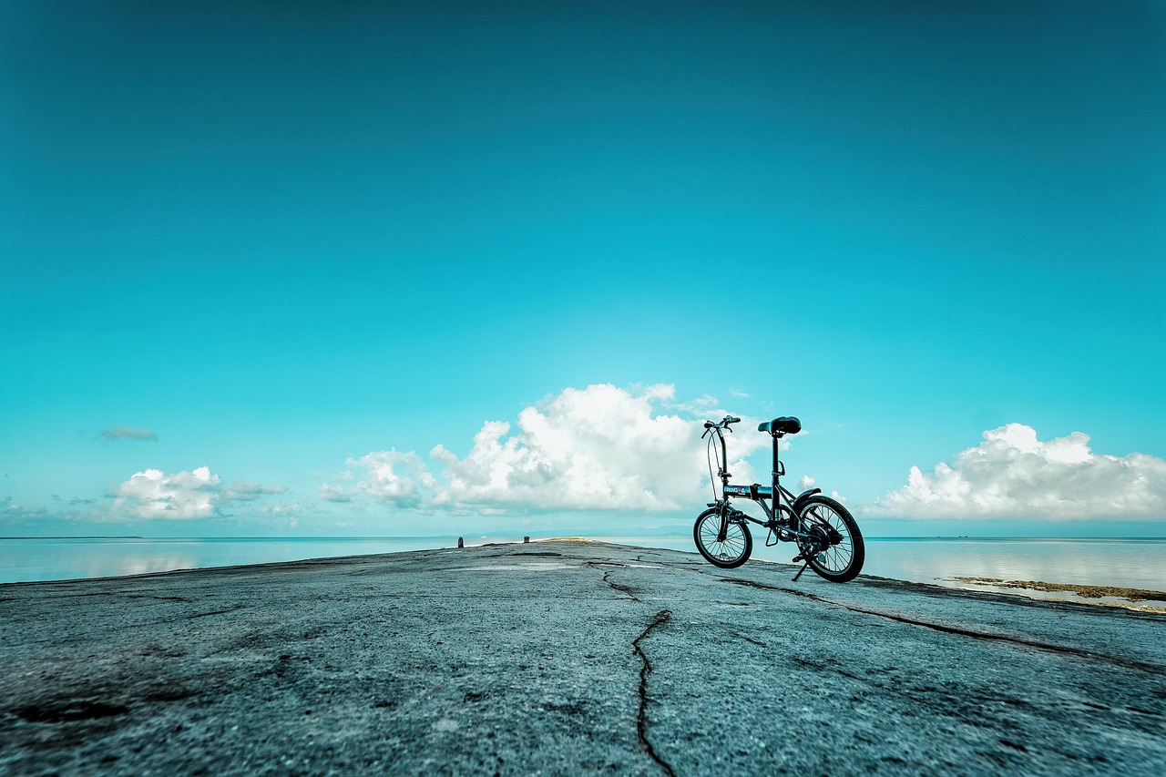 A cracked concrete pier running out over calm shallow water, a folding bicycle parked at its edge under a clear turquoise sky