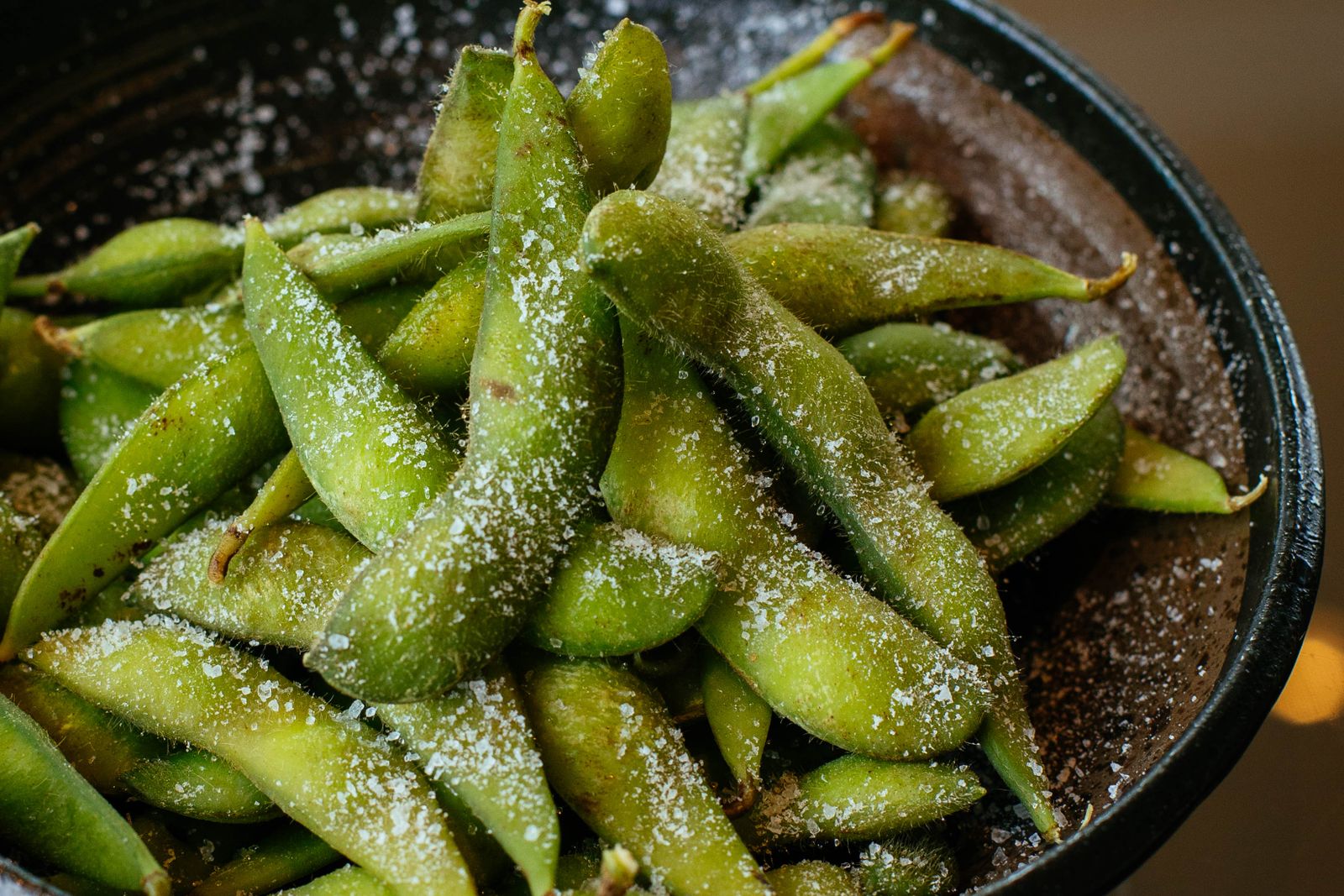 Salted edamame pods heaped in a small black bowl, seen from above.