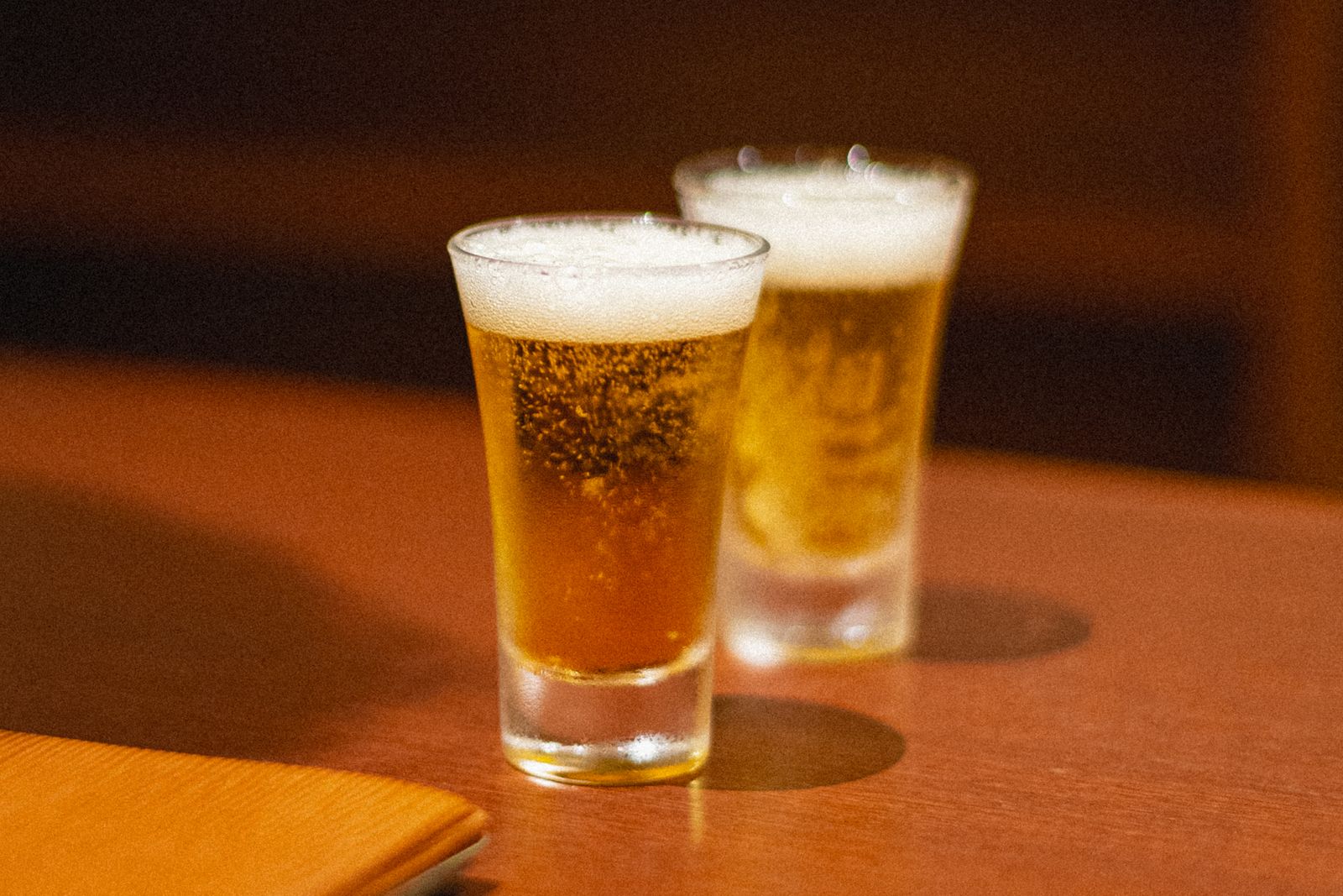 Two small glasses of beer with foam, standing on a wooden counter.