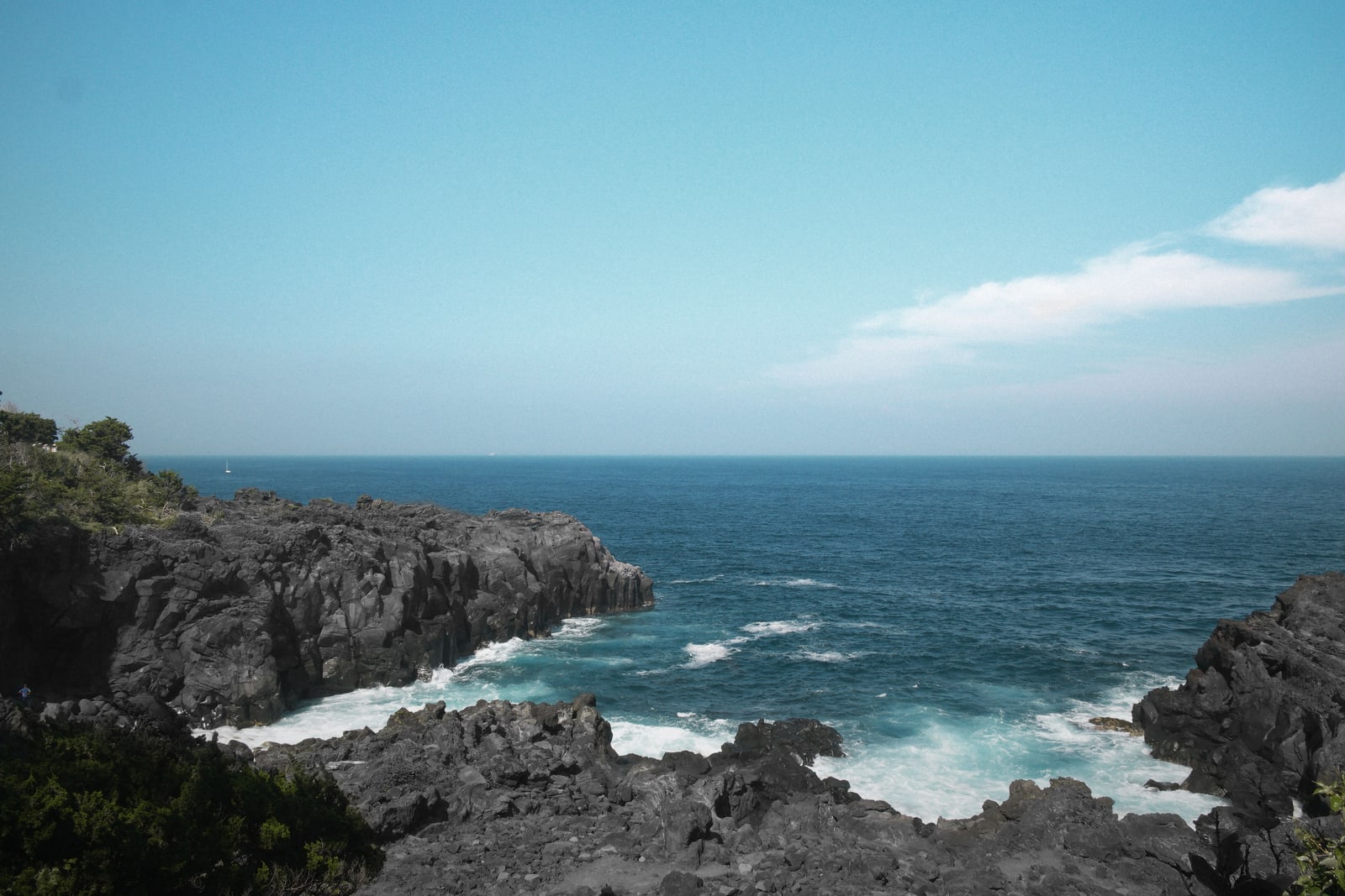 Black volcanic rock cliffs and white surf on an open sea coast under a blue sky