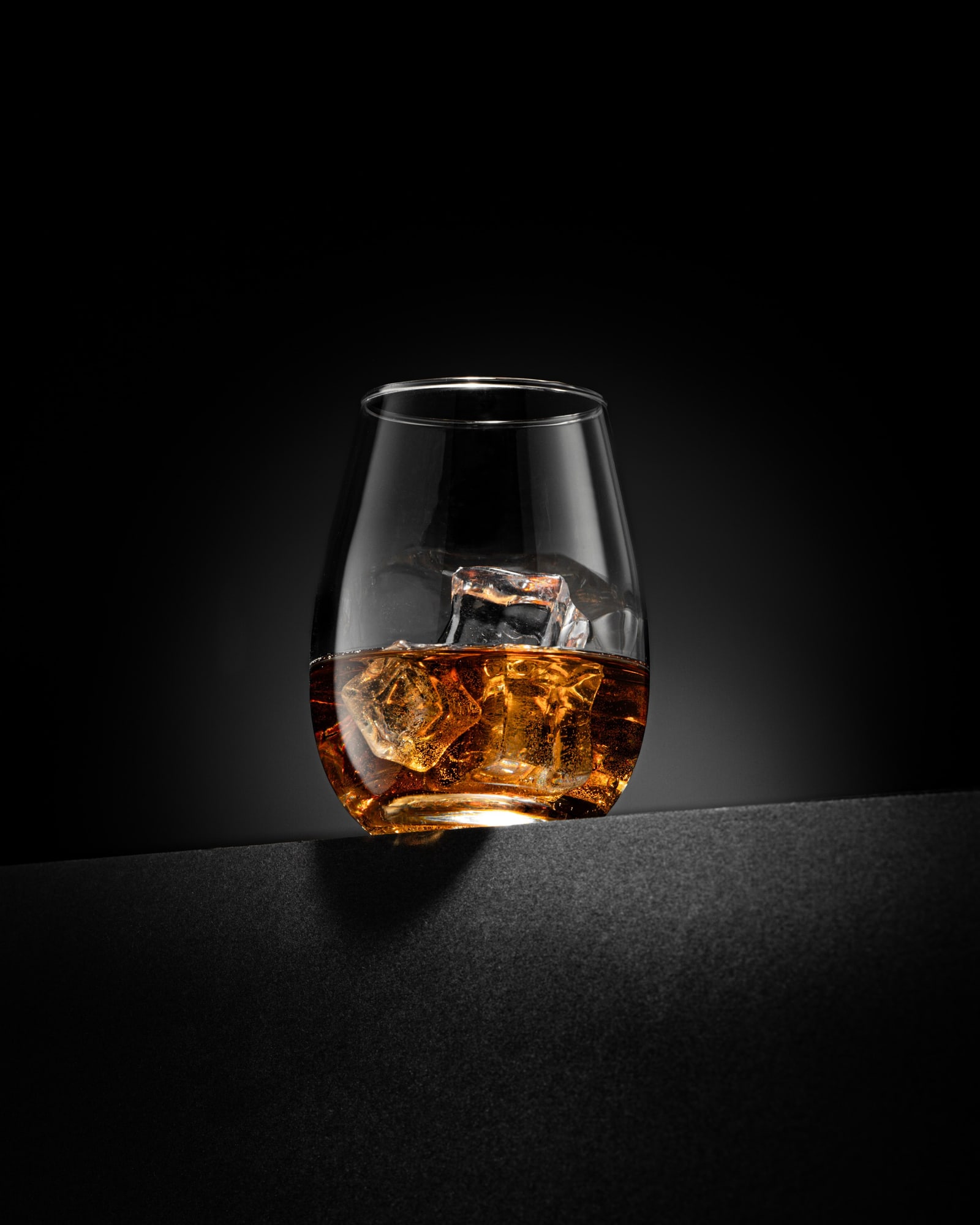 A glass of whisky over ice cubes against a black background.