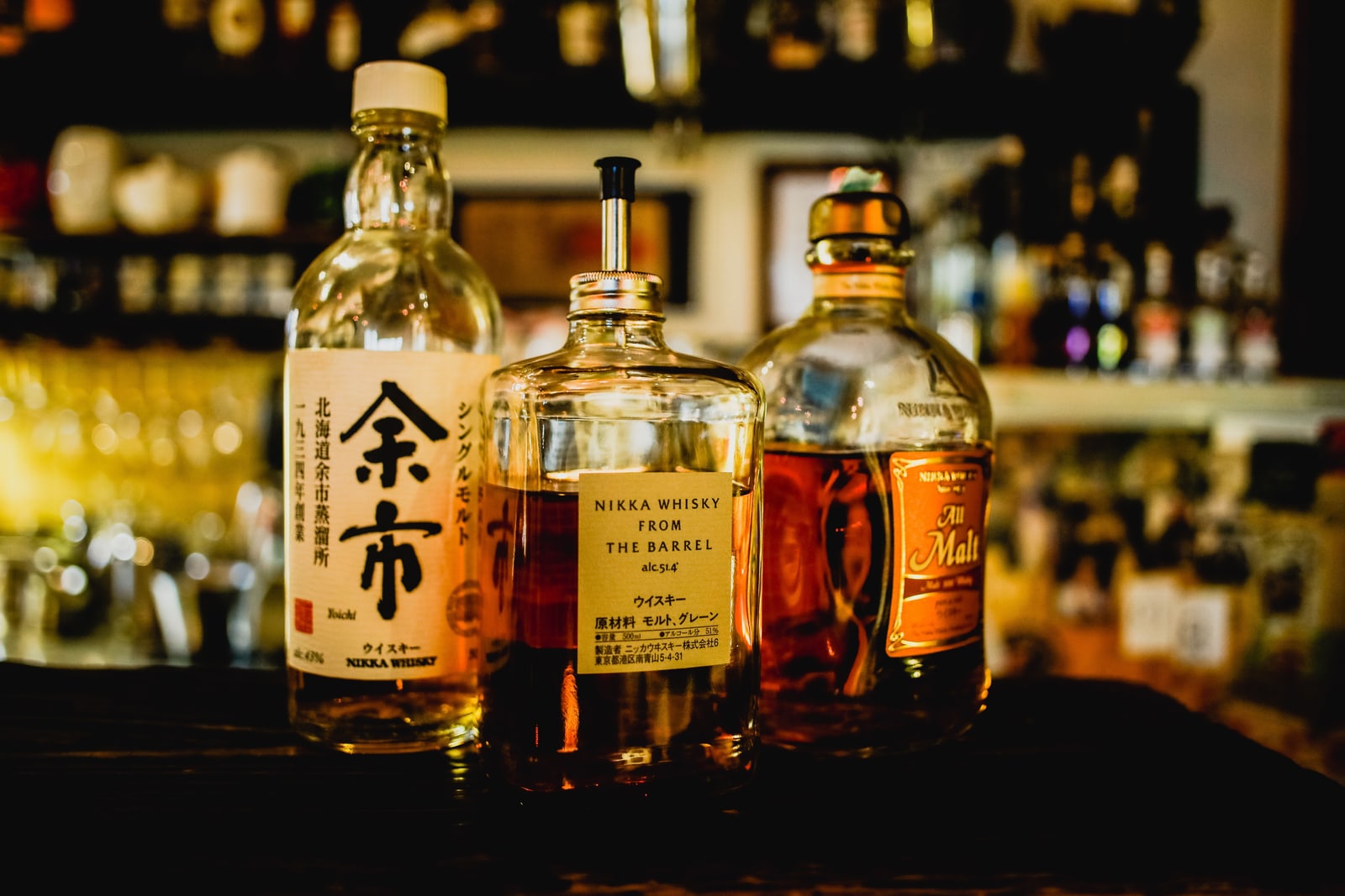 Three Nikka whisky bottles — Yoichi single malt, From the Barrel and All Malt — standing on a dim bar counter.