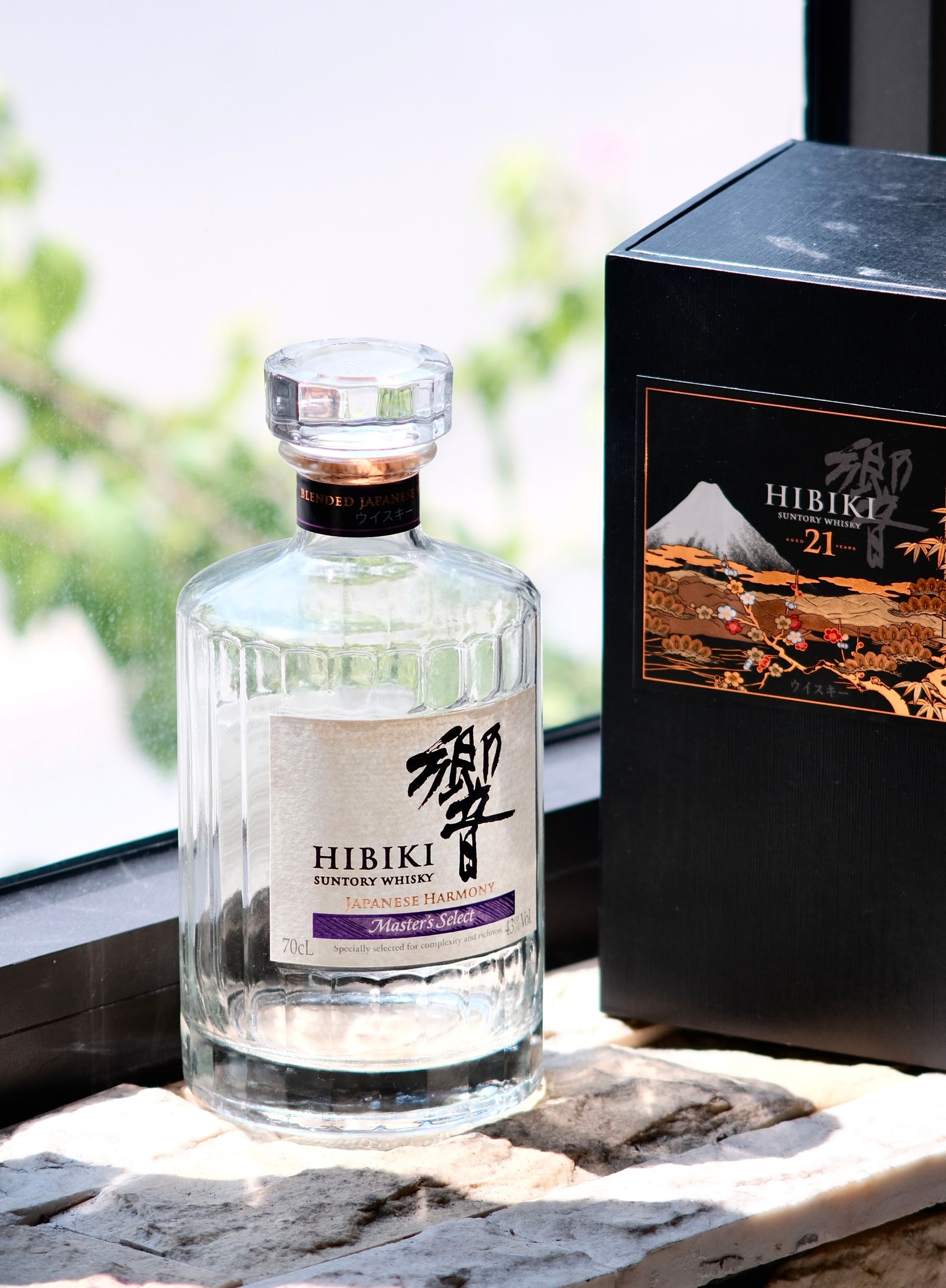 A bottle of Hibiki Japanese Harmony Master's Select on a sunny stone window sill beside a Hibiki 21 box.