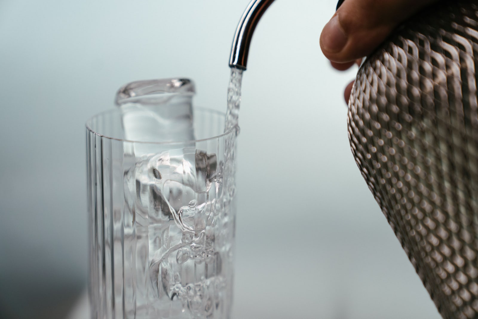 Soda water being poured from a siphon over ice in a tall glass.