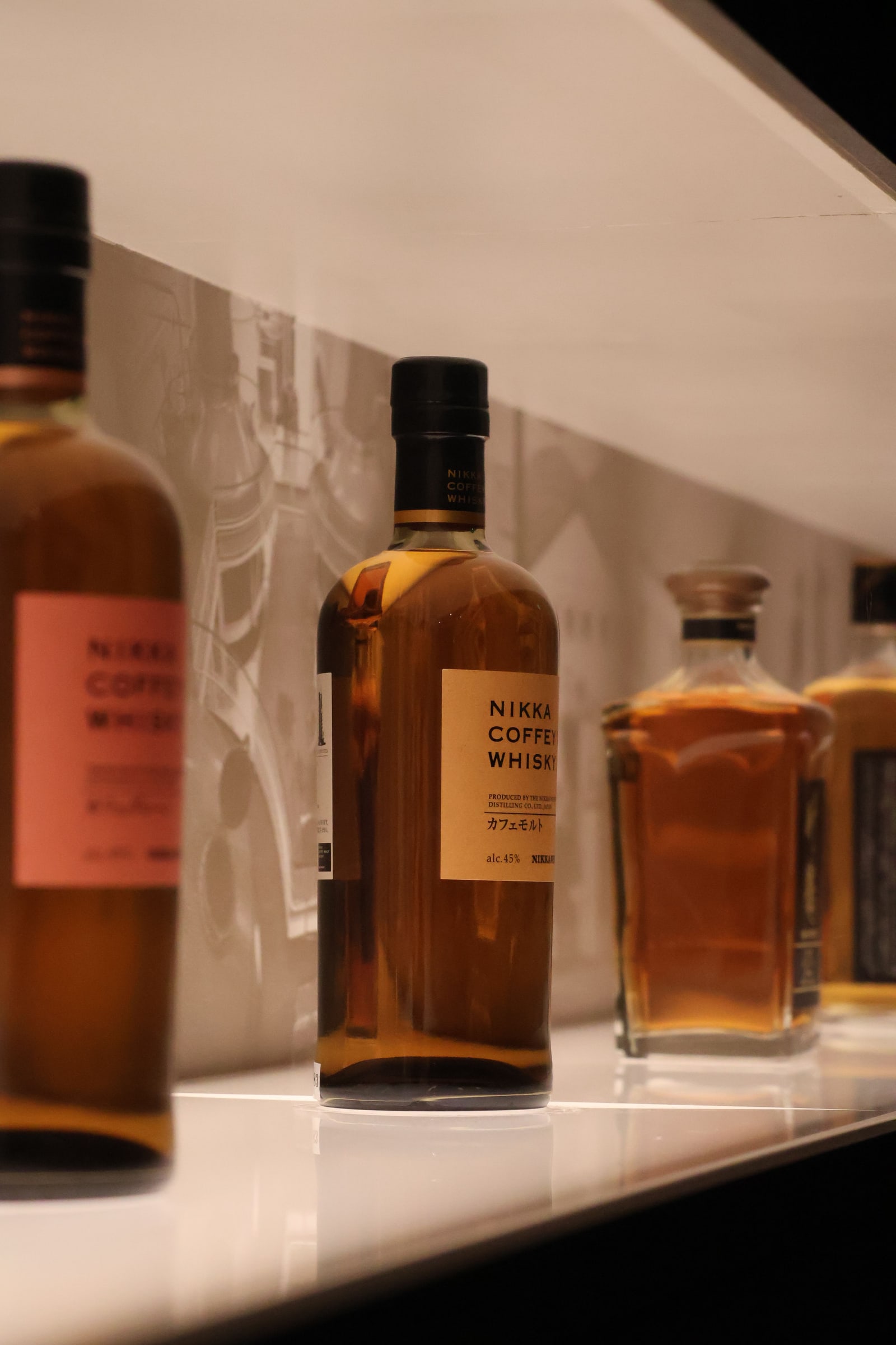 Nikka Coffey-series whisky bottles on a lit display shelf, a Coffey Malt bottle in focus.