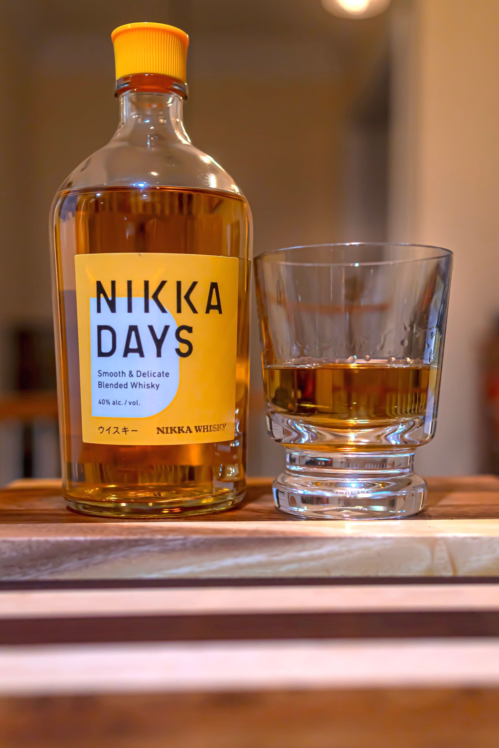 A bottle of Nikka Days beside a poured glass of whisky on a wooden board.