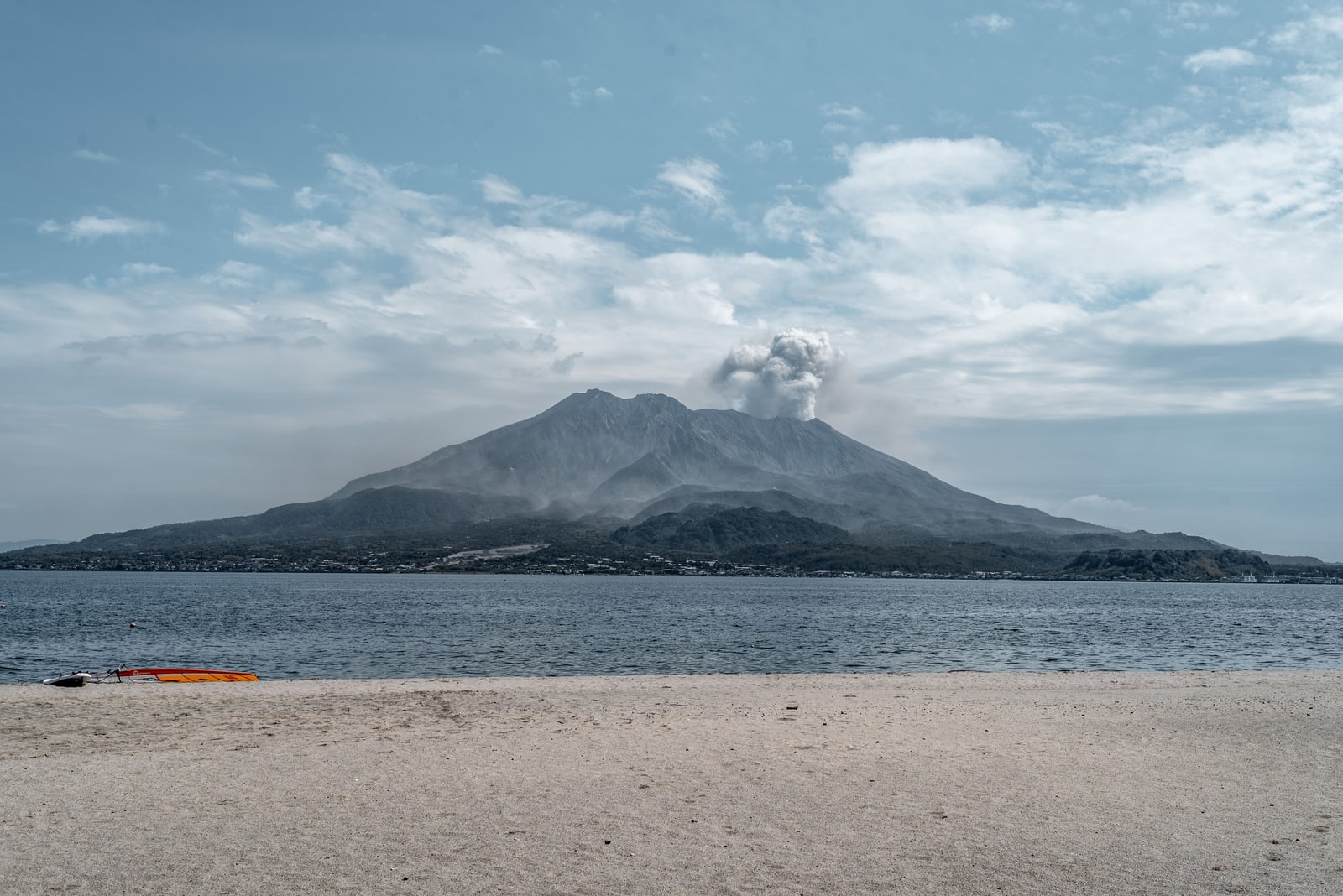 Sakurajima with a smoke plume, seen across Kagoshima Bay from a sand beach
