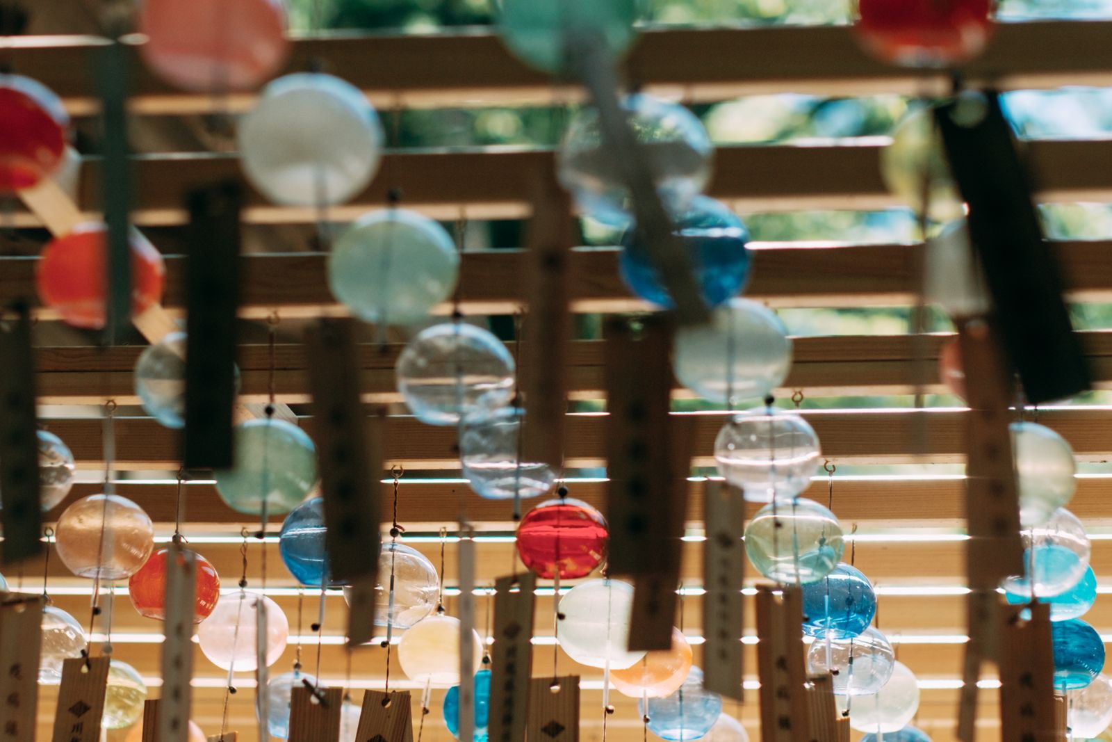 Rows of glass wind chimes in red, blue and clear glass with wooden tags, hanging from a wooden frame