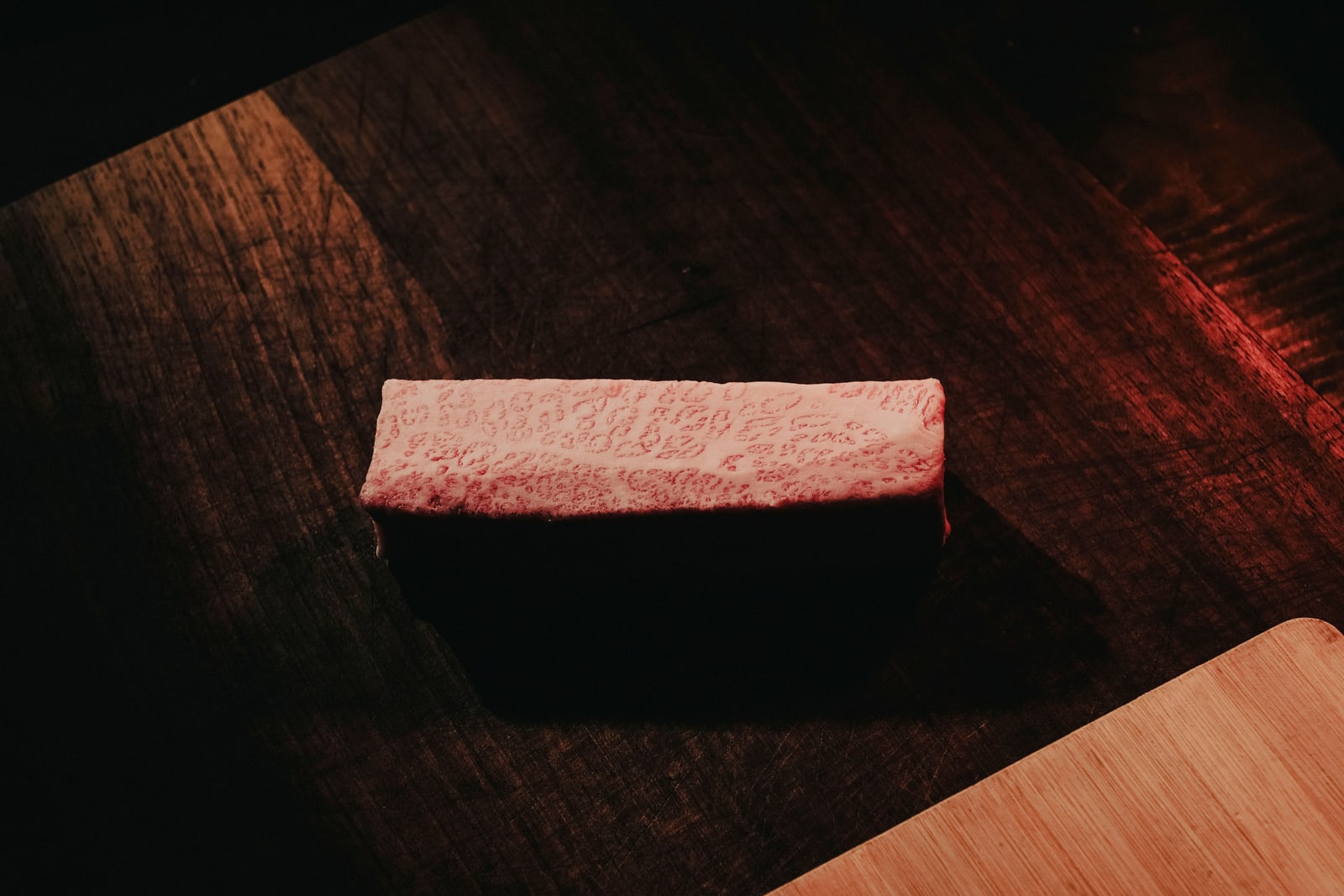 A single rectangular block of raw beef, pale with heavy fine marbling, on a dark wooden table in low warm light.