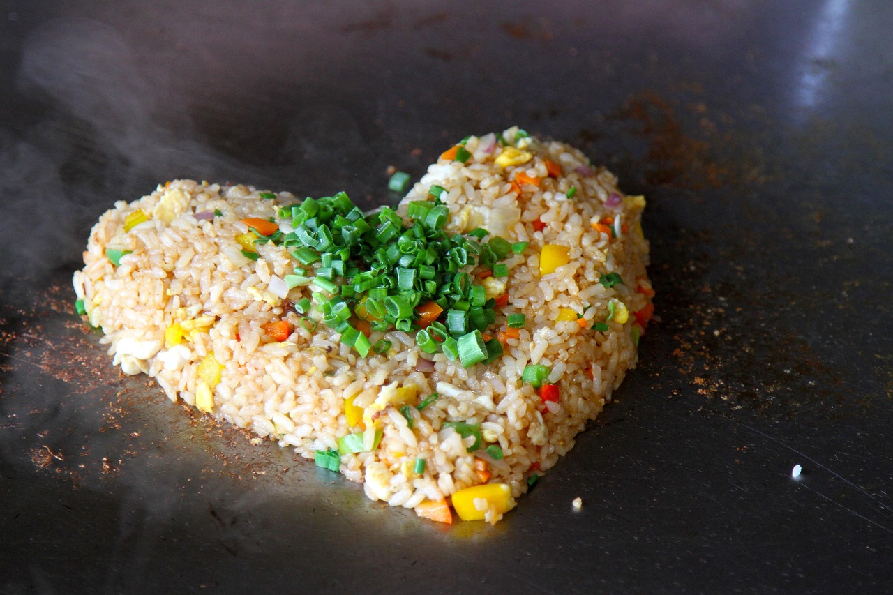 Fried rice shaped into a heart on a dark steel griddle, chopped green onion and diced vegetables on top.