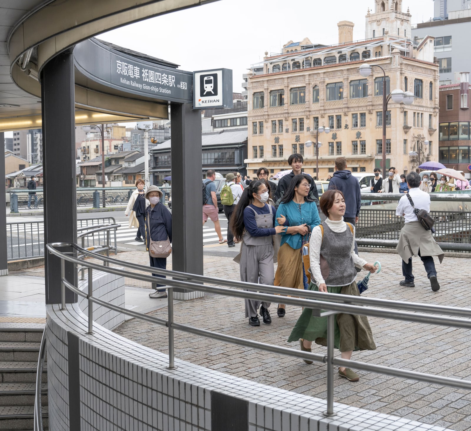 A curved stairway entrance with a station sign reading Keihan Gion-Shijo, pedestrians on the pavement.