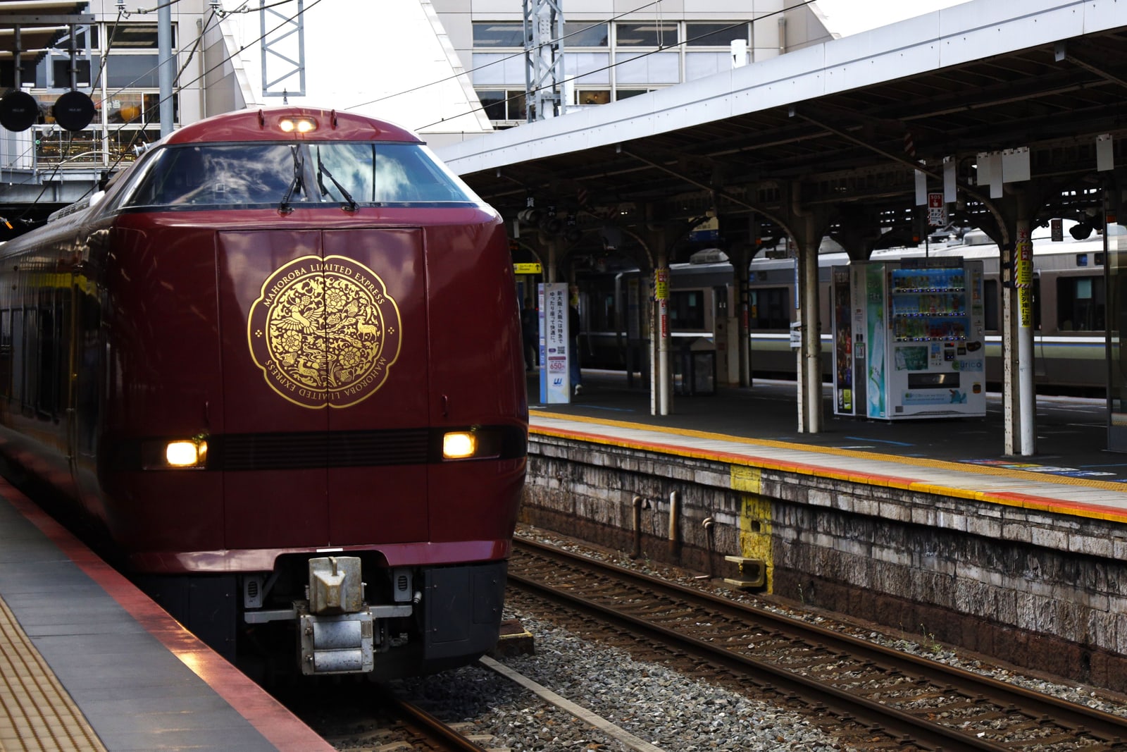 A deep-red limited express train with a gold emblem on its nose, waiting at a platform at Kyoto Station.