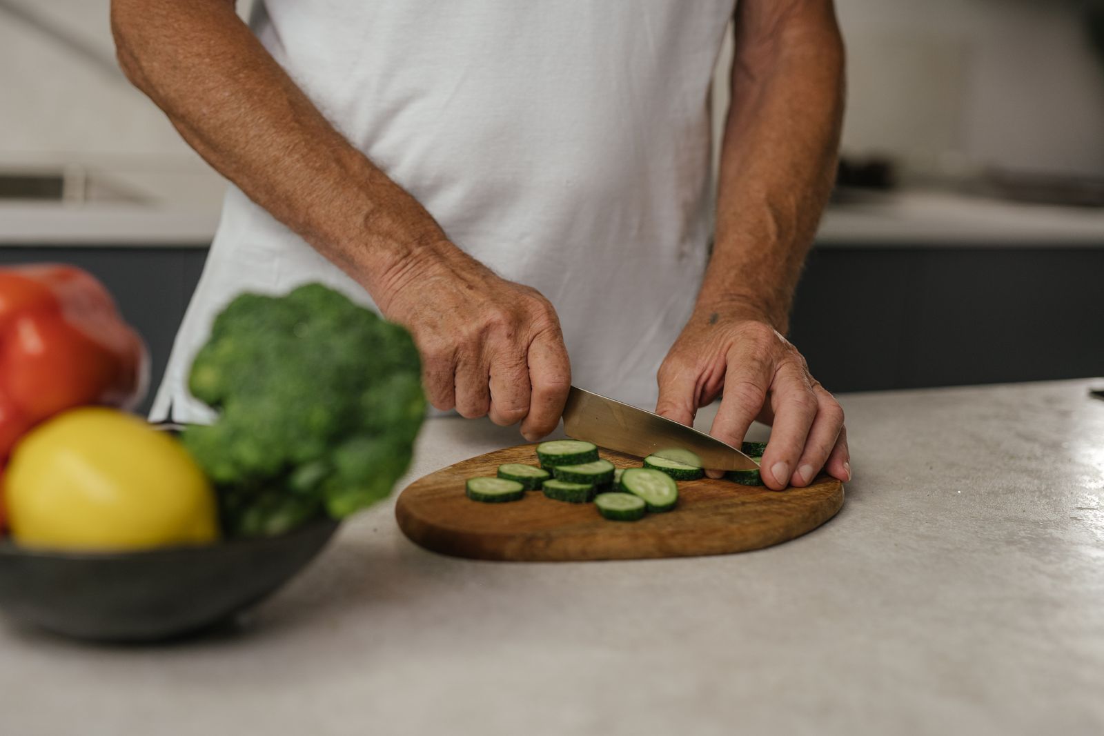 Hands slicing cucumber straight down on a wooden board.