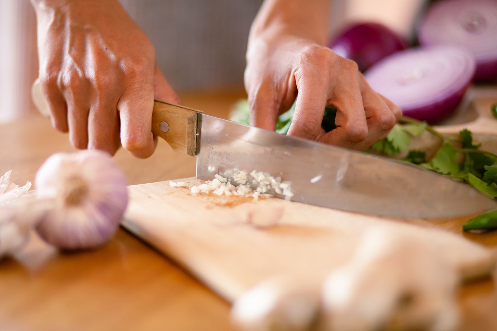 Hands chopping garlic and onion on a wooden board.