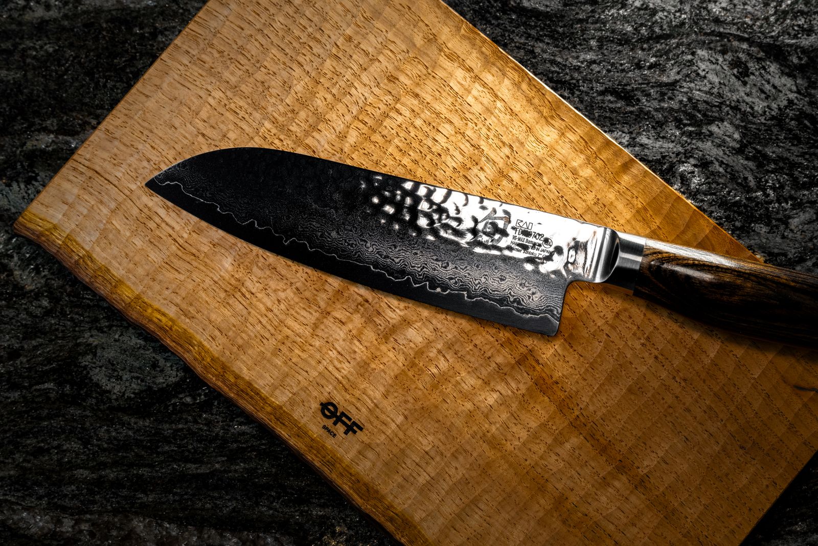 A santoku knife with a hammered Damascus blade resting on a wooden board, the blade stamped MADE IN JAPAN.