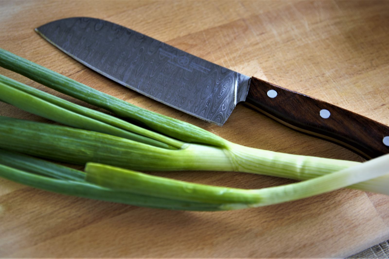 A blade at rest on a board beside cut spring onion, wooden handle in frame.