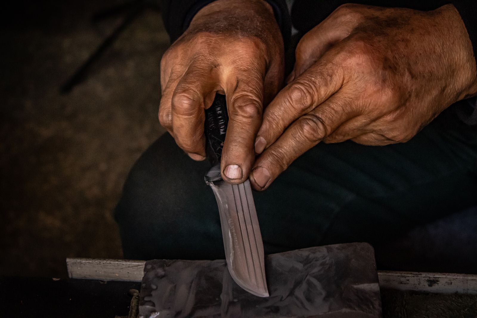Hands drawing a knife edge across a wet sharpening stone.