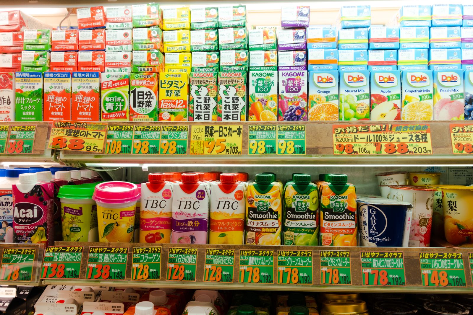 A Japanese chilled drinks shelf, every tag printed with a large pre-tax figure and a smaller tax-included total underneath.