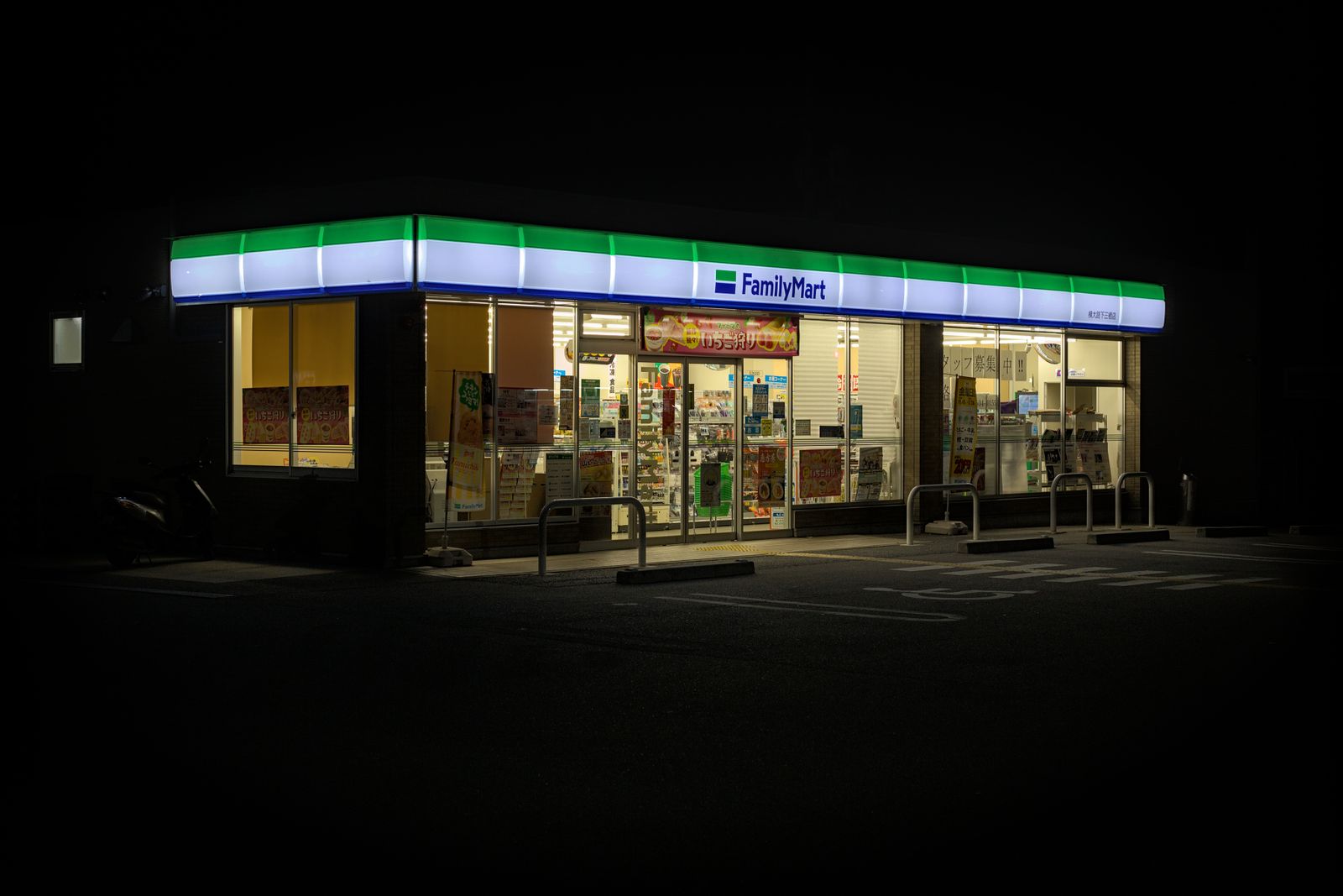A FamilyMart storefront lit green and blue at night in Kyoto, with a recruiting notice in the window.