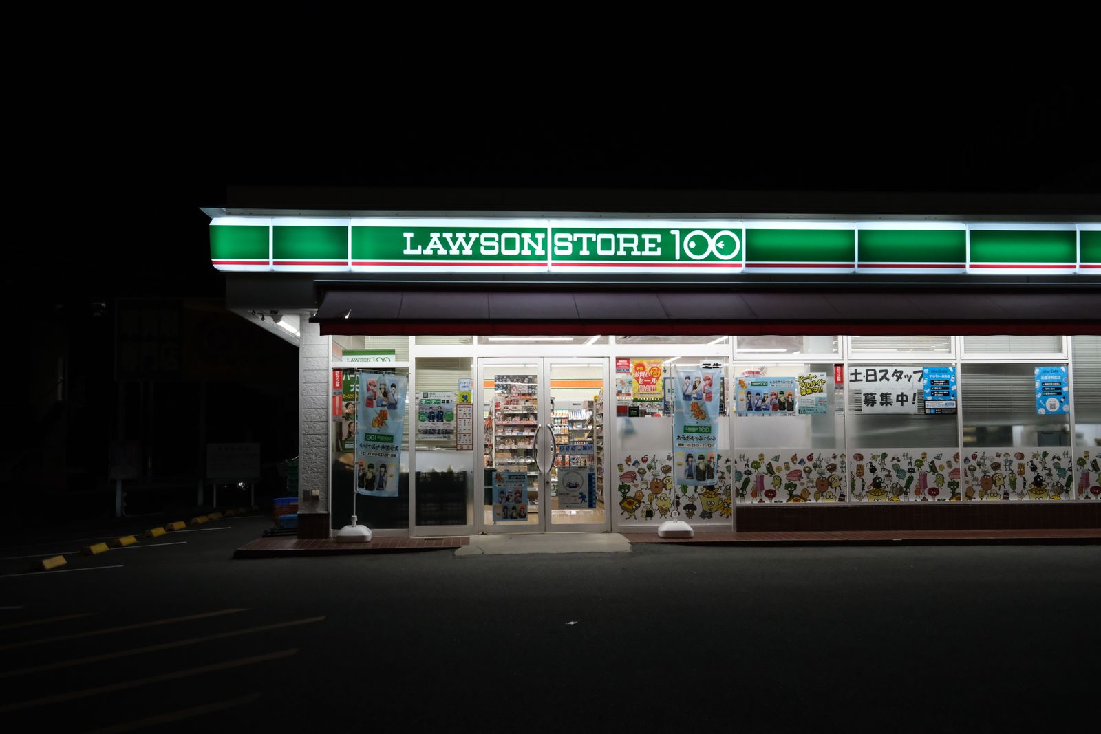 A Lawson Store 100 lit up at night in Toyohashi, Aichi, with campaign notices across the windows.