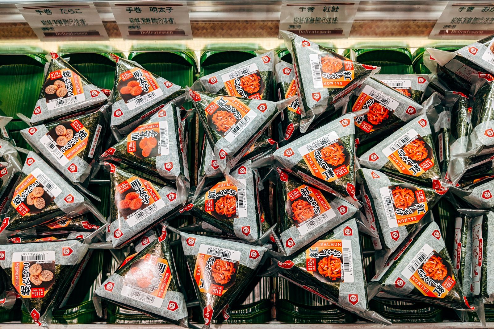 A shelf of packaged hand-rolled onigiri in a Japanese store, each with a Japanese label and a yen price printed on the wrapper.