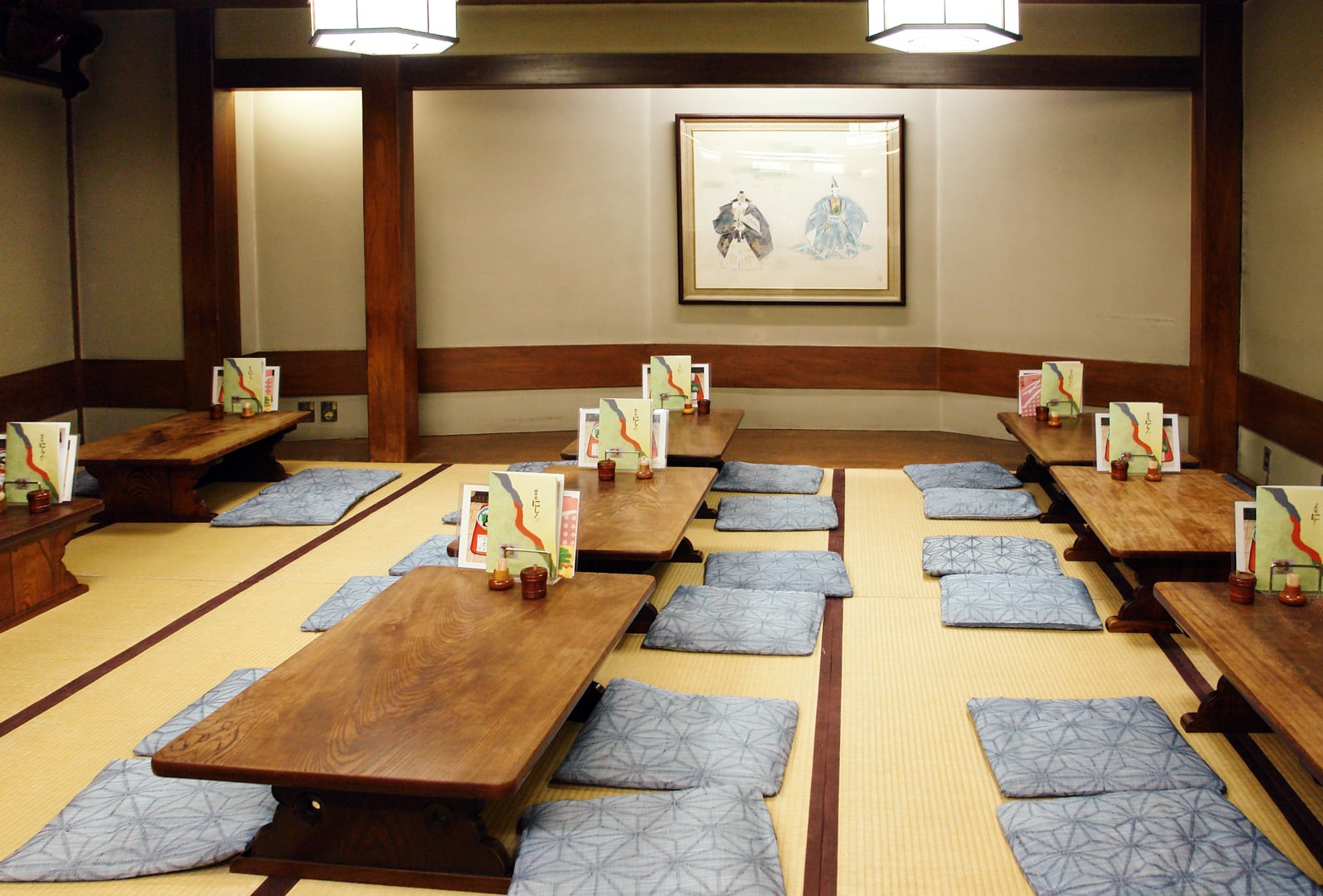 Rows of low wooden tables with blue cushions on tatami in a Japanese dining room, a menu stand on each table.