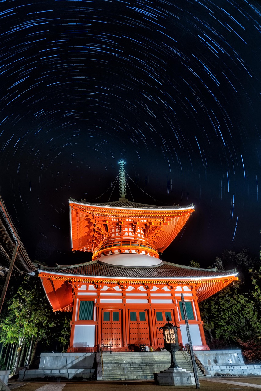 A vermilion two-story pagoda lit at night under circular star trails in a long exposure.