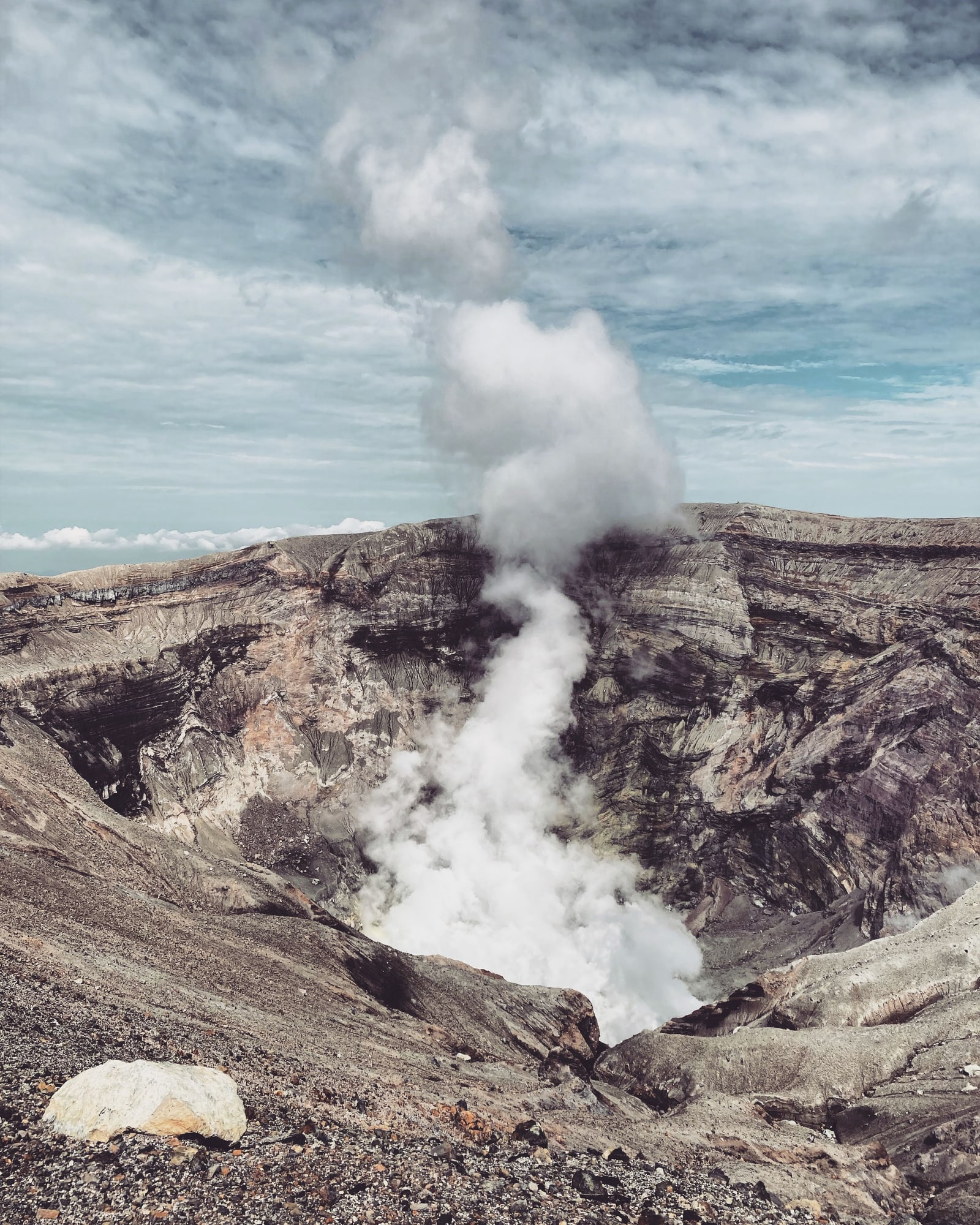 Steam rising from the Nakadake crater of Mt. Aso, its layered grey and brown walls below a streaky sky