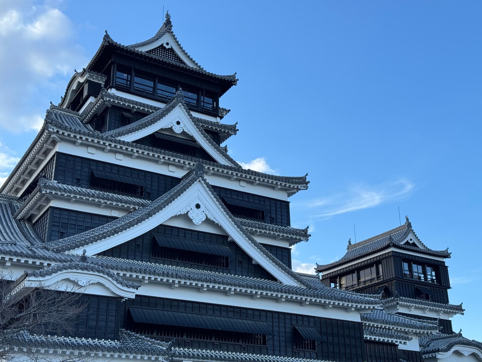 The black-and-white main and small keeps of Kumamoto Castle under a deep blue sky