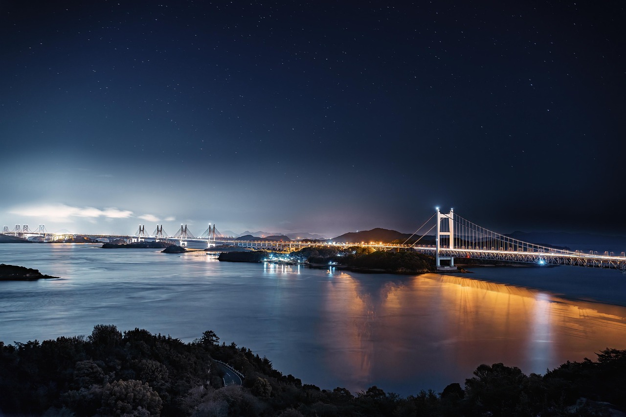 A chain of bridges lit at night across the Seto Inland Sea under a starry sky