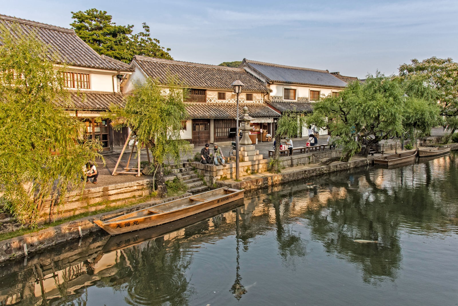 White-walled storehouses along the canal in the Kurashiki Bikan Historical Quarter, willows on the bank and wooden boats moored below