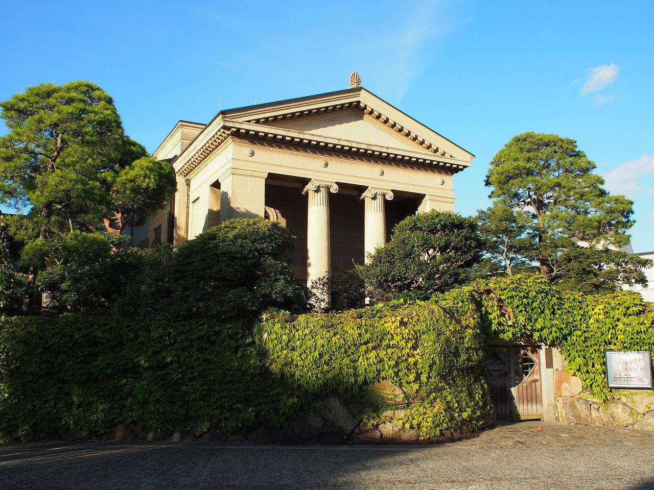 The Greek-temple front of the Ohara Museum of Art main building, with Ionic columns behind an ivy-covered wall and pines