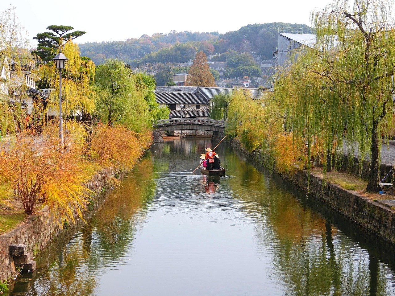 A canal lined with willows in autumn, a small boat poled toward a stone bridge