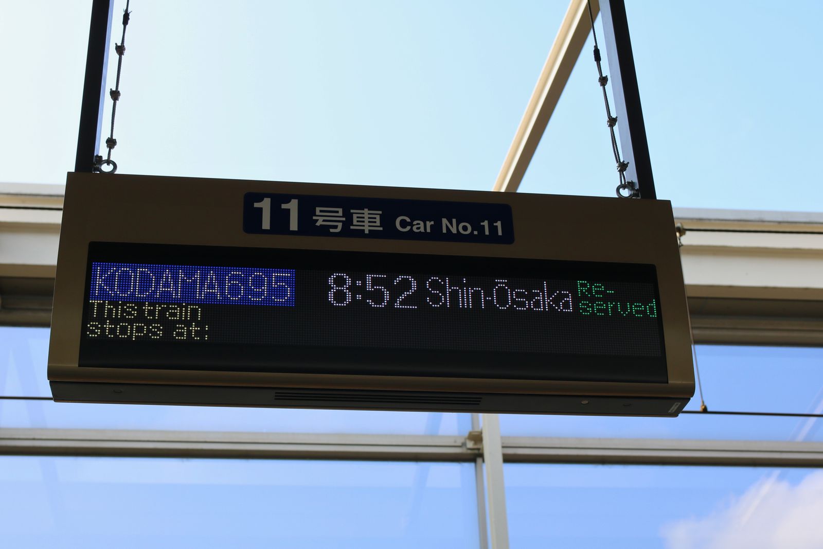 A platform car-position indicator against open sky, its dot matrix showing a train name, a time and a destination.