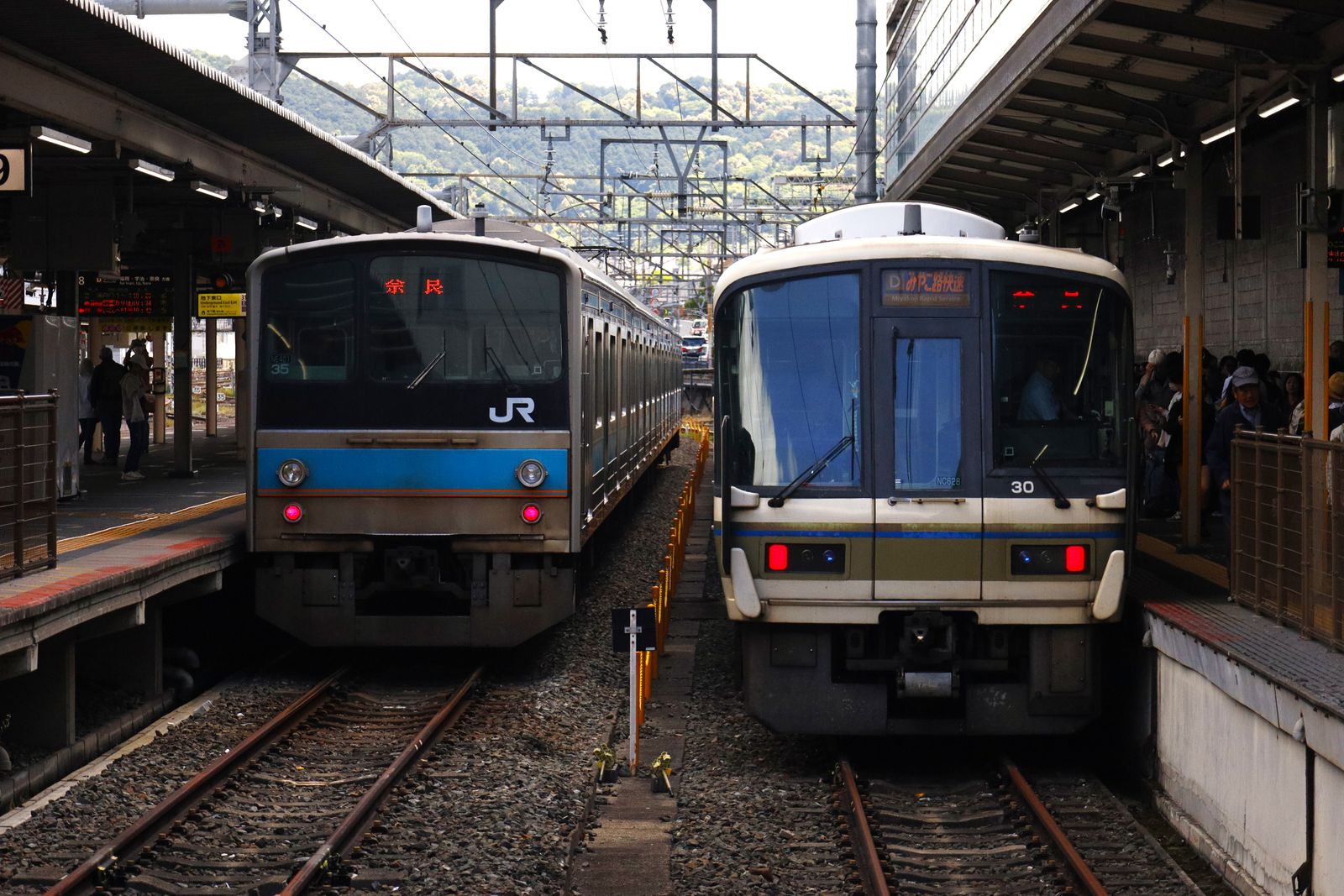 Two JR commuter trains standing nose to nose at adjacent platforms in Kyoto Station, one destination board reading Nara and the other the Miyakoji Rapid Service.