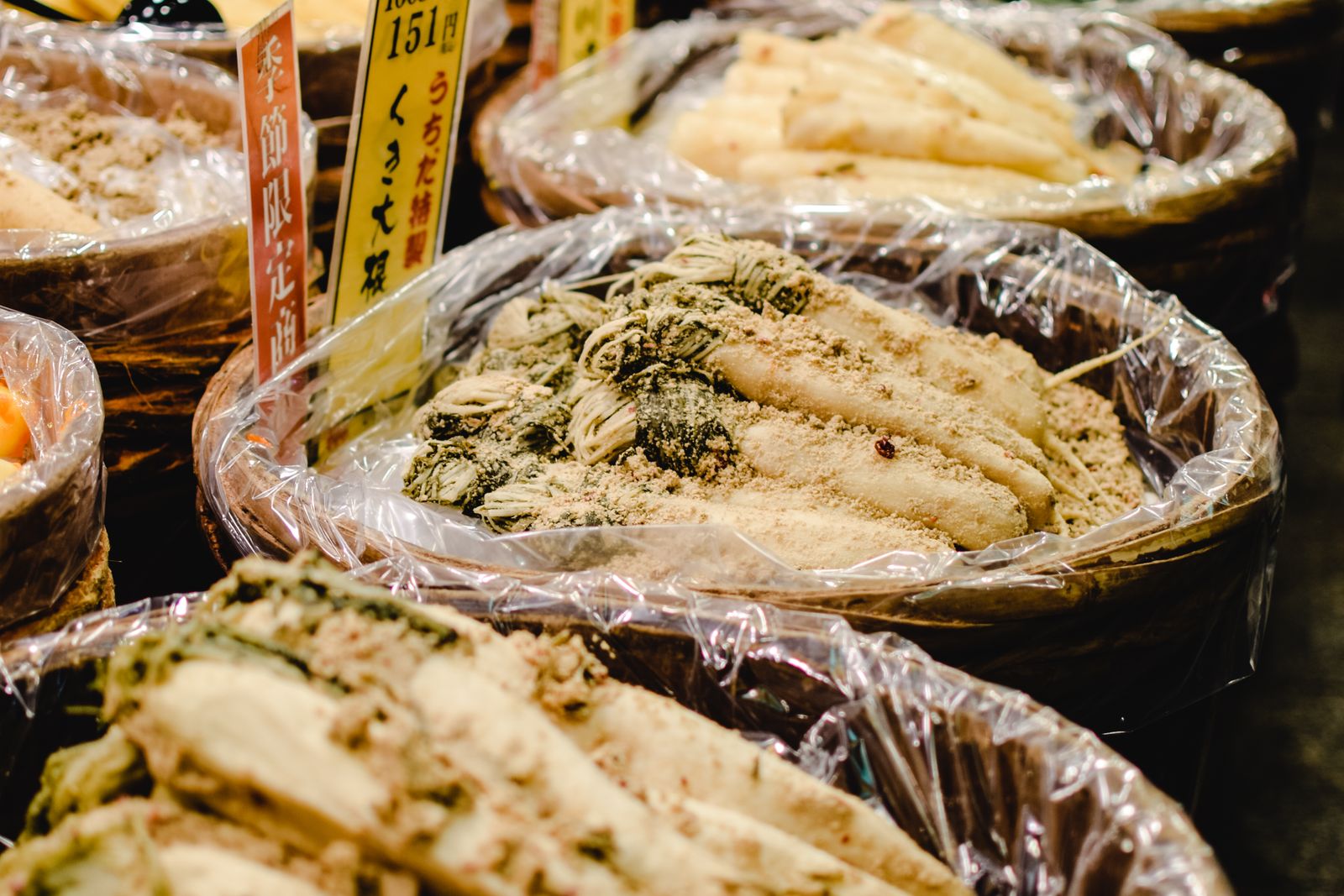 Tubs of bran-pickled daikon and greens with handwritten Japanese cards at Nishiki Market.