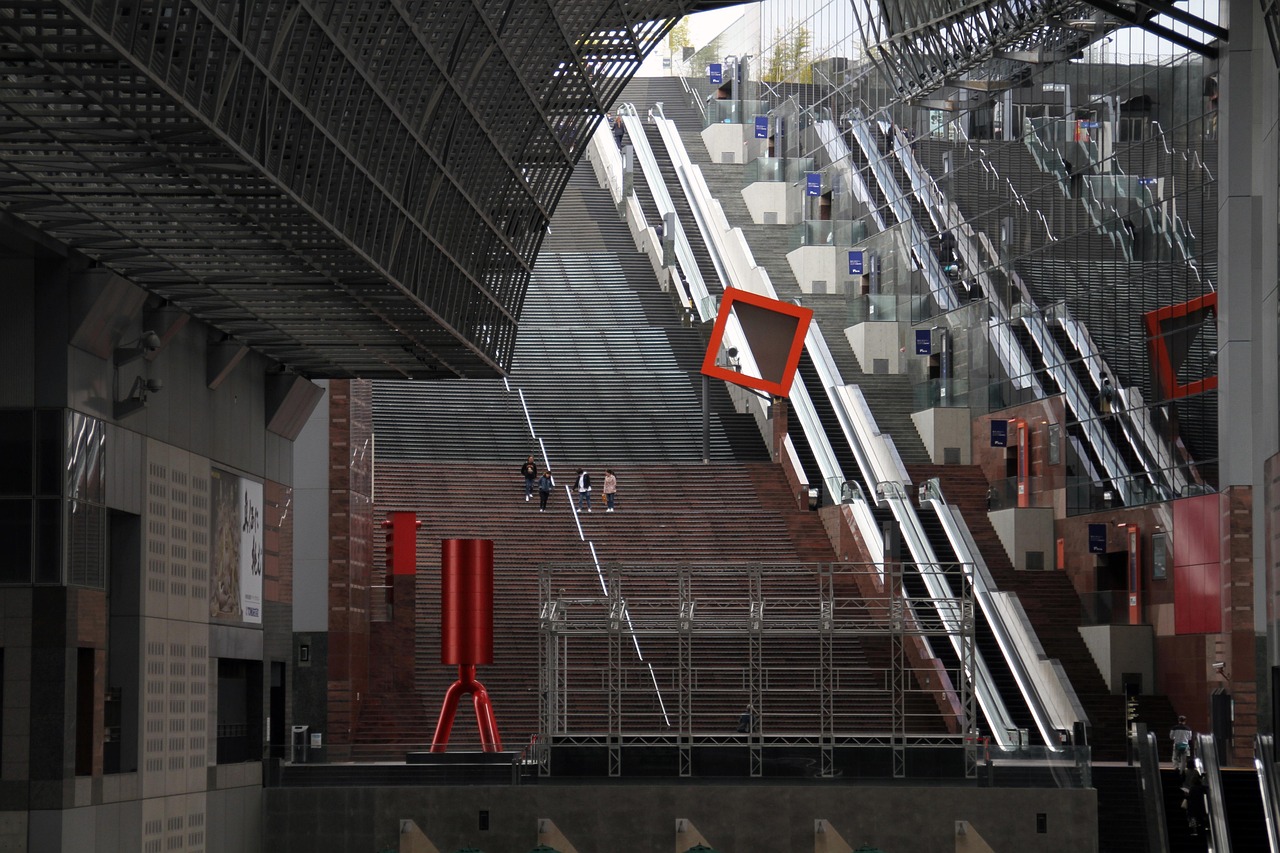 The wide Great Stairs inside the glass-and-steel Kyoto Station building, escalators beside the steps and a red sculpture at the foot