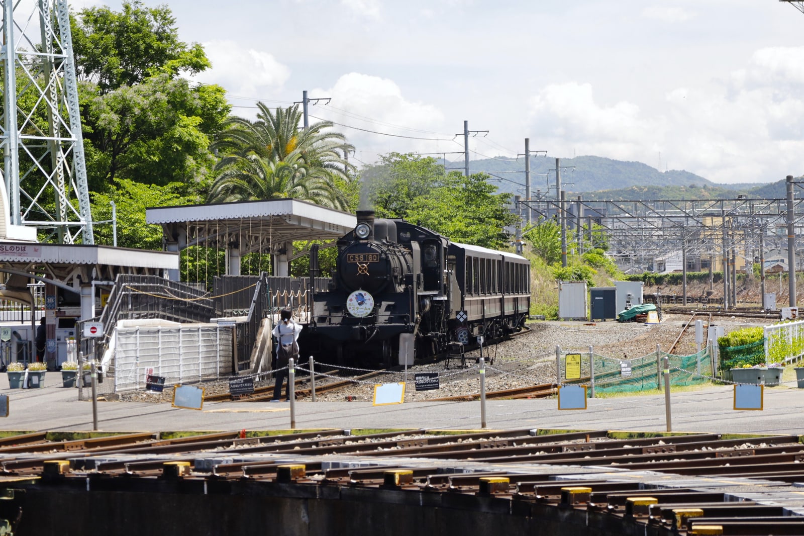A black steam locomotive and two passenger cars at a boarding platform beside a turntable at the Kyoto Railway Museum