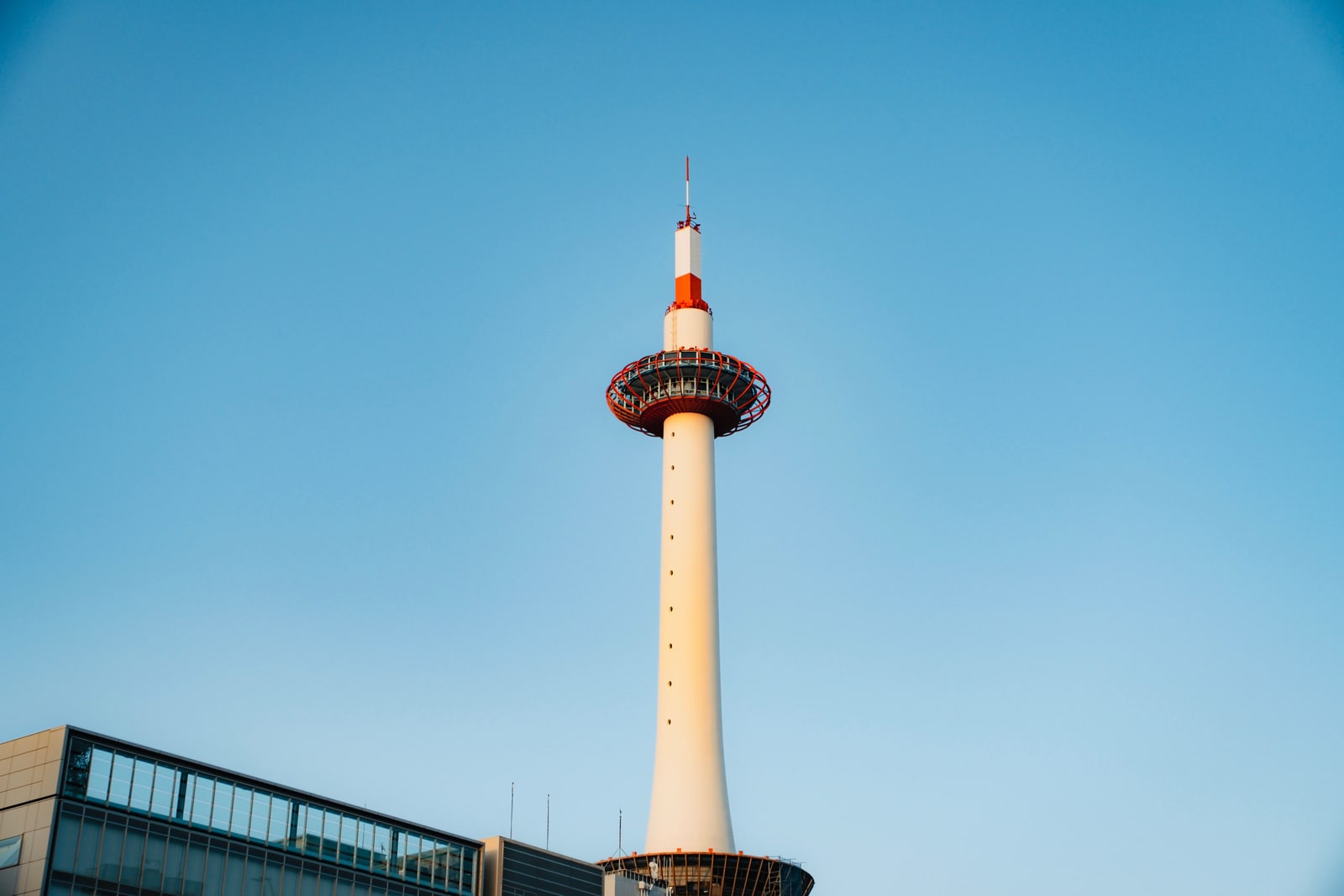 Kyoto Tower, a white tower with a red lattice observation ring, against a blue sky