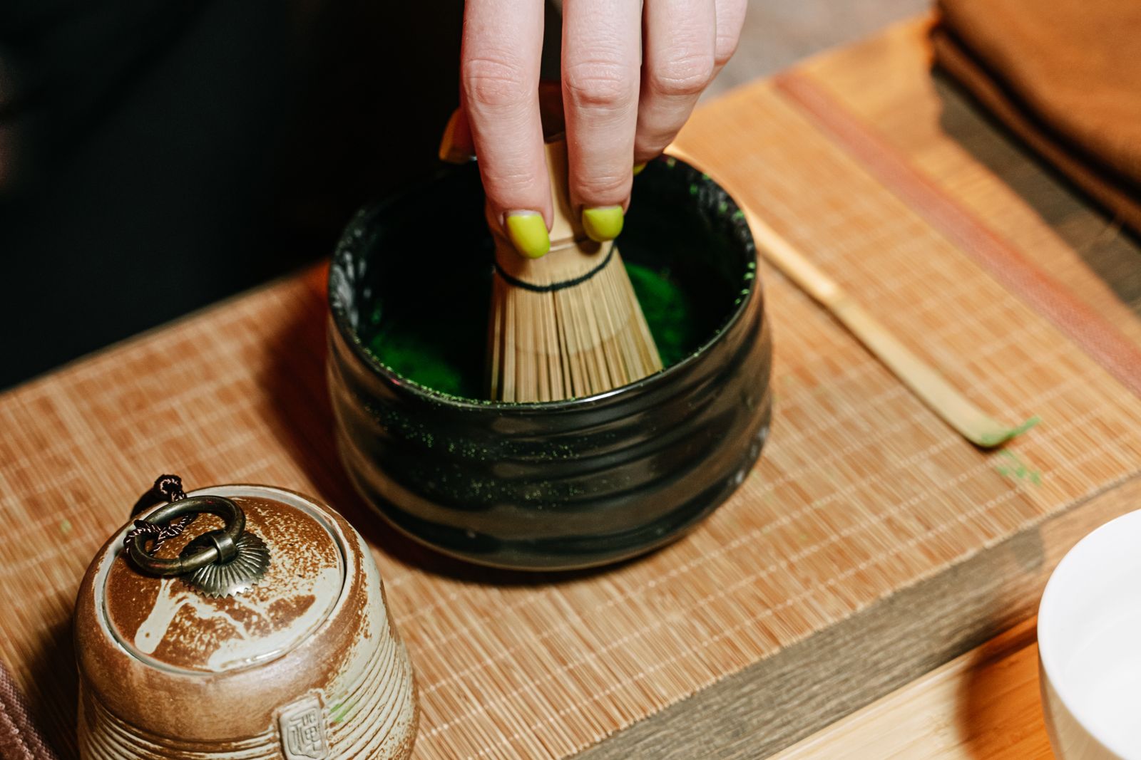 A hand whisking matcha in a bowl, the surface breaking into foam.