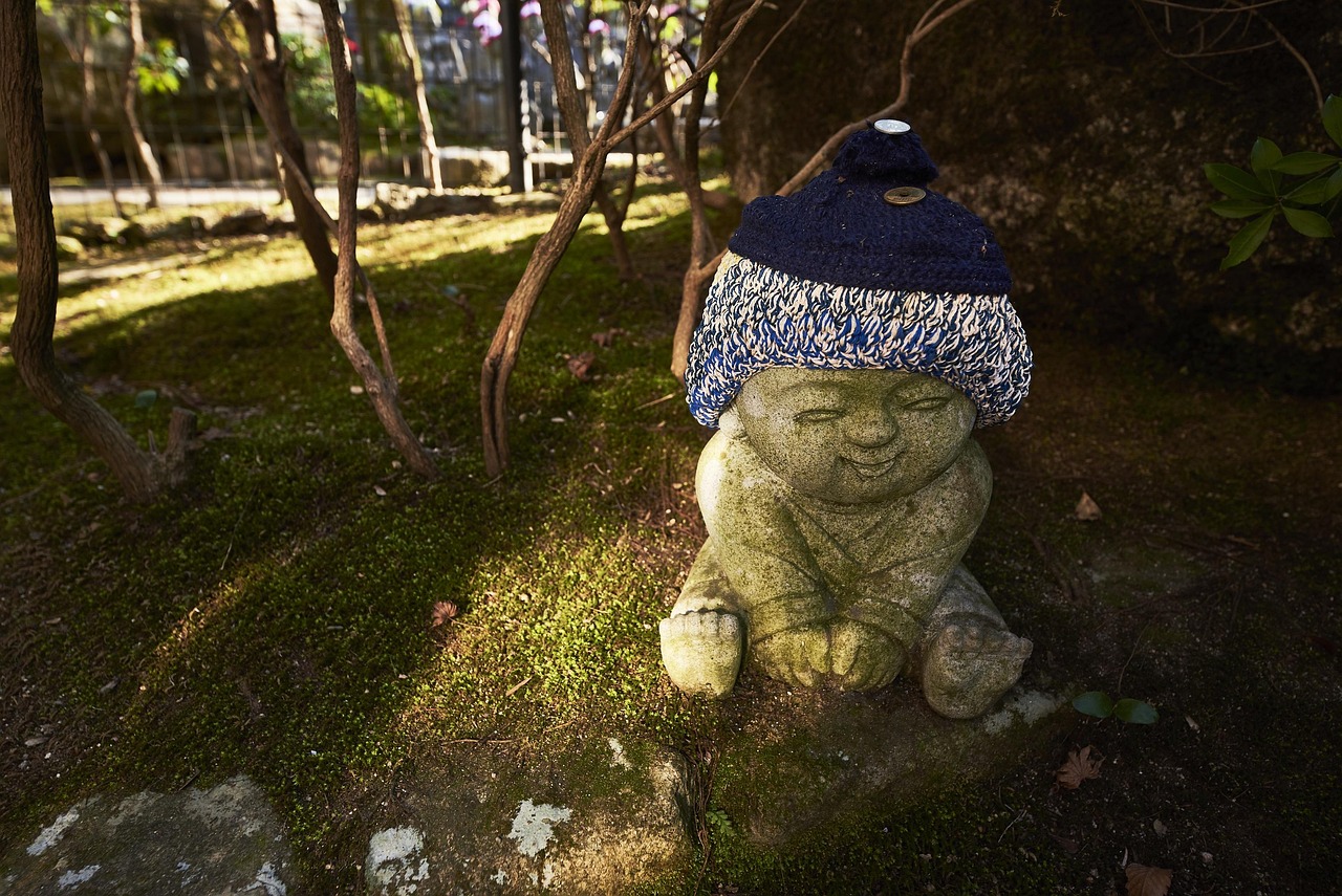 A small mossy stone jizo in a knitted blue-and-white cap at Daisho-in, Miyajima
