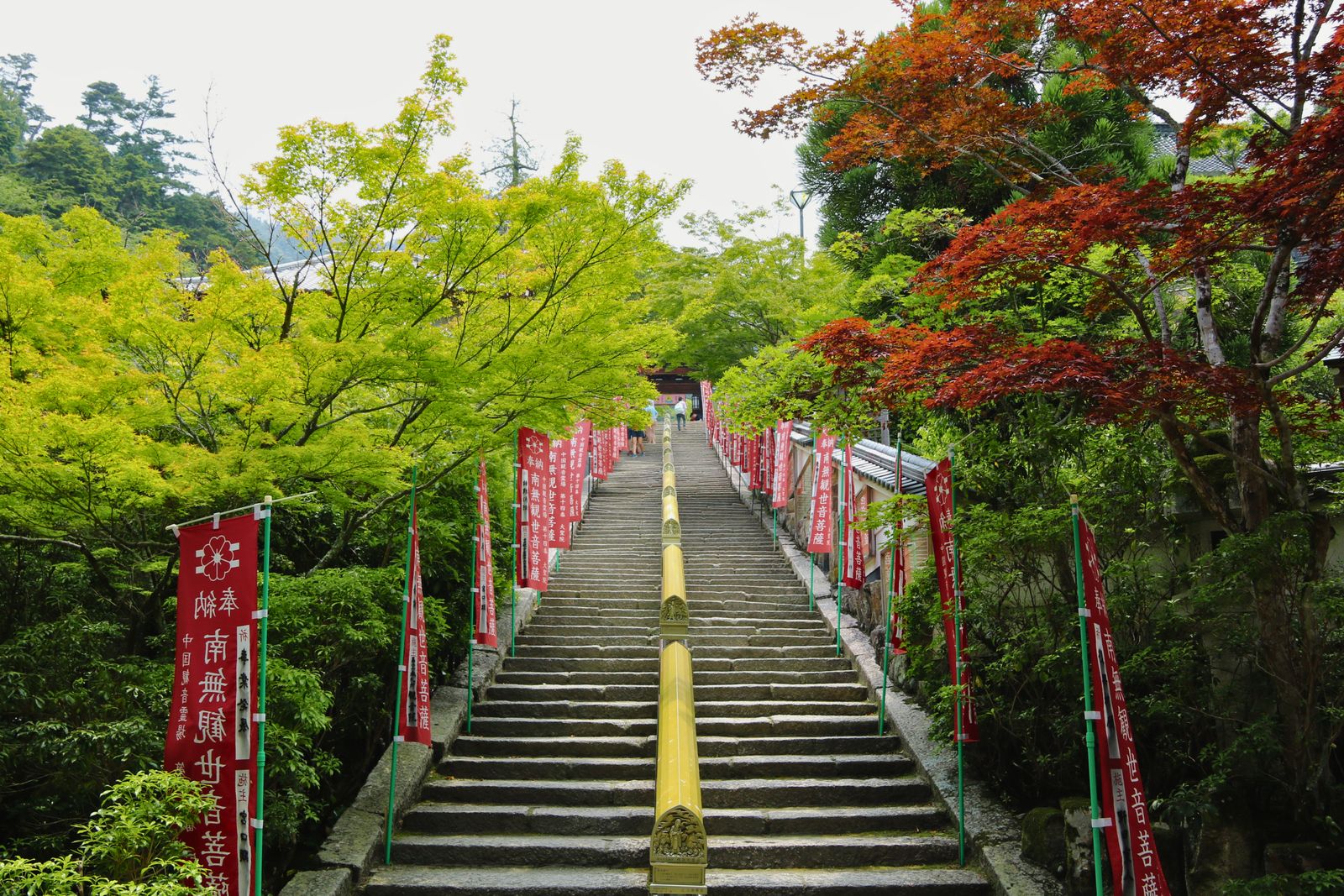 Stone steps at Daisho-in on Miyajima with a handrail of brass sutra cylinders, red banners and maples on both sides