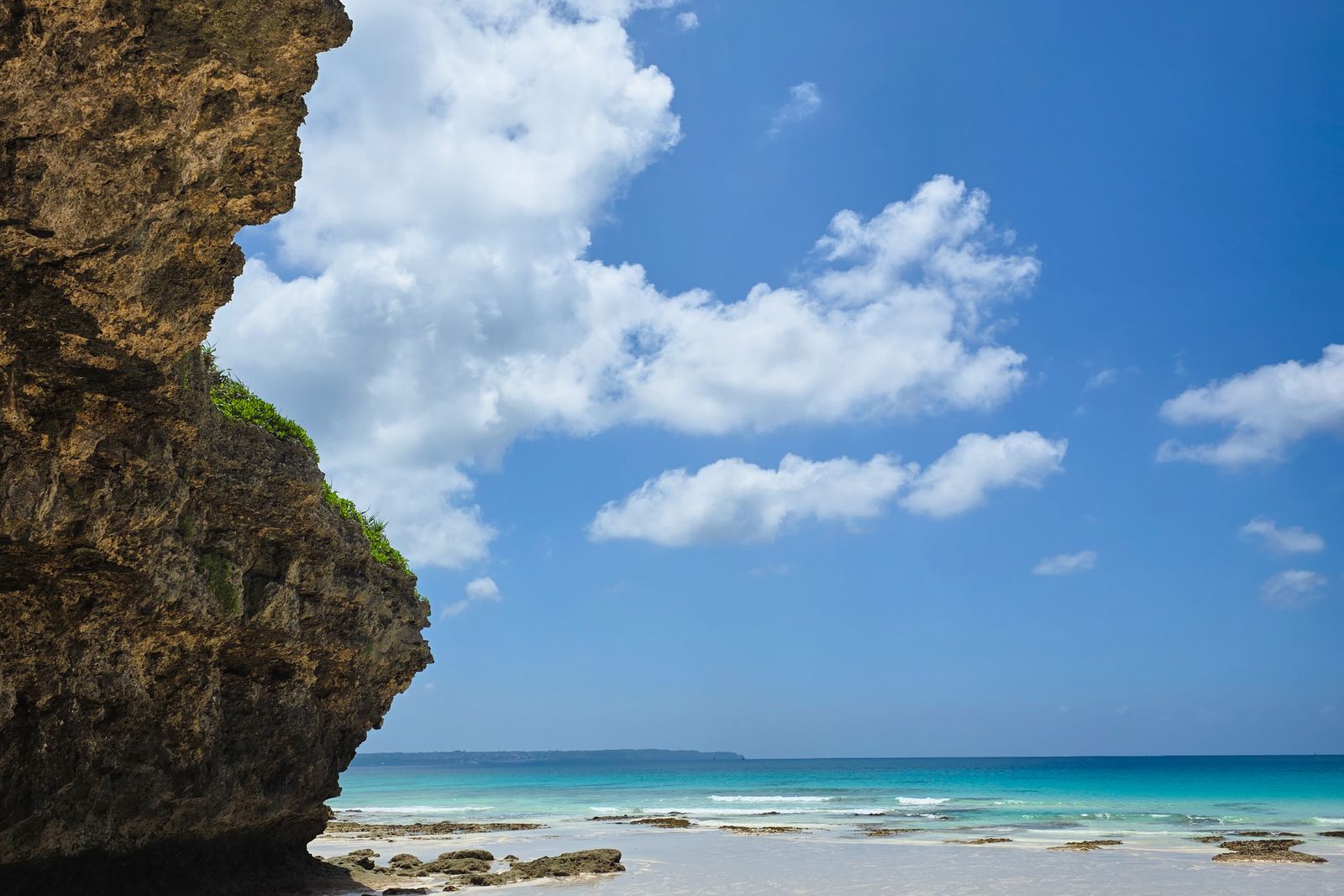 A limestone cliff above a white-sand beach and turquoise sea on Miyakojima